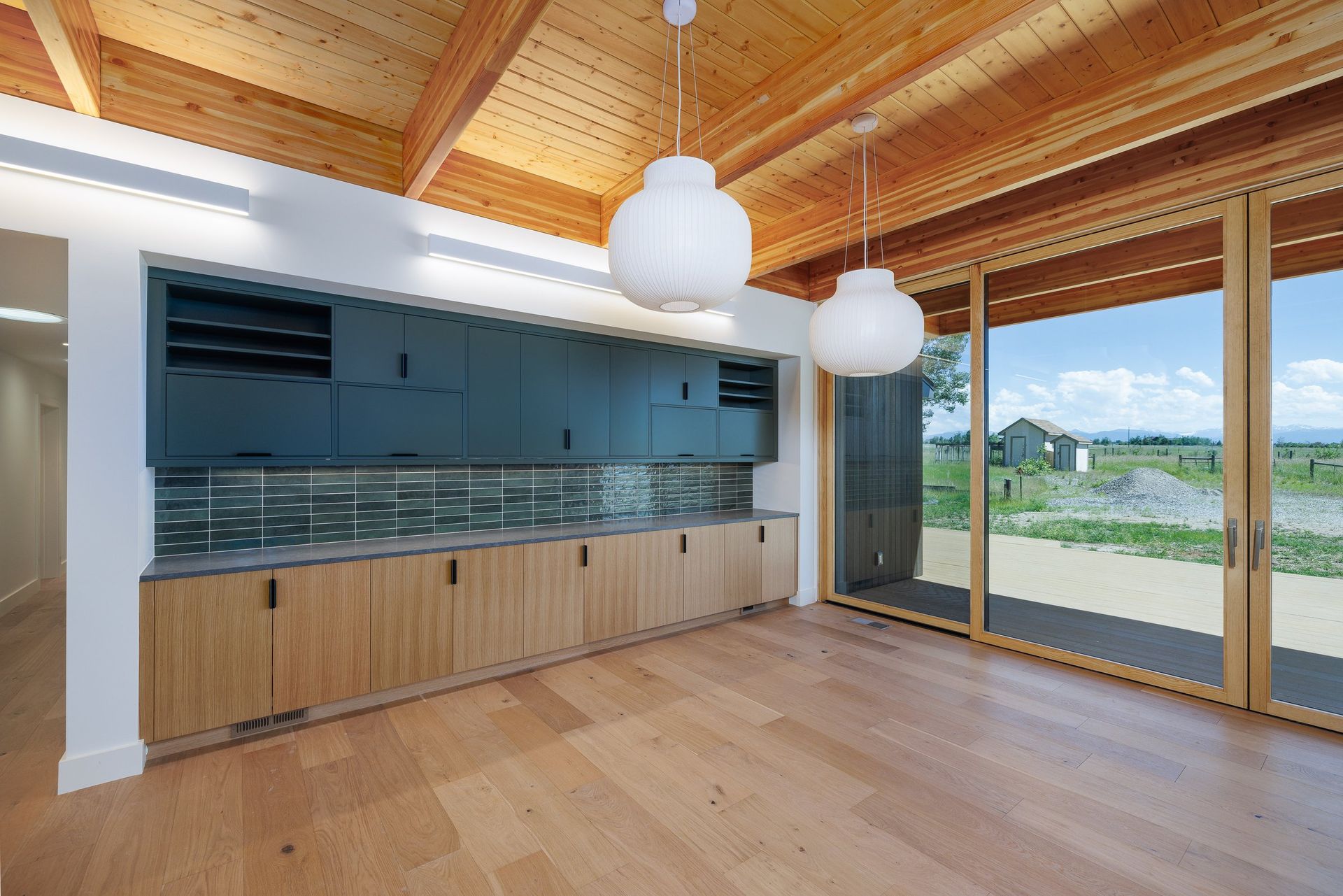A modern kitchen with light wood cabinets, dark upper cupboards, a glass backsplash, and a large sliding glass door.
