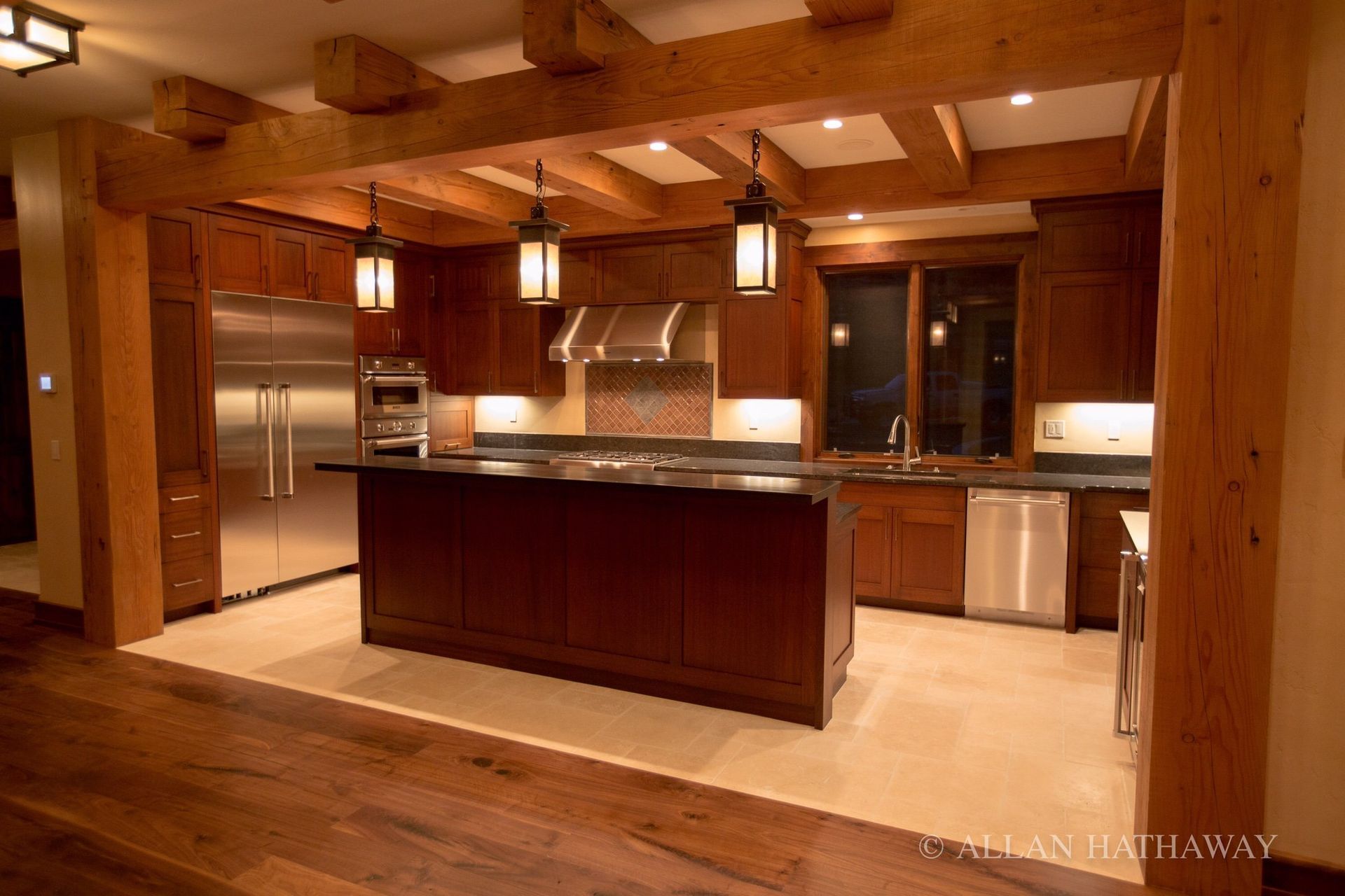A kitchen with wood cabinetry, a large central island, stainless steel appliances, and prominent decorative ceiling beams.