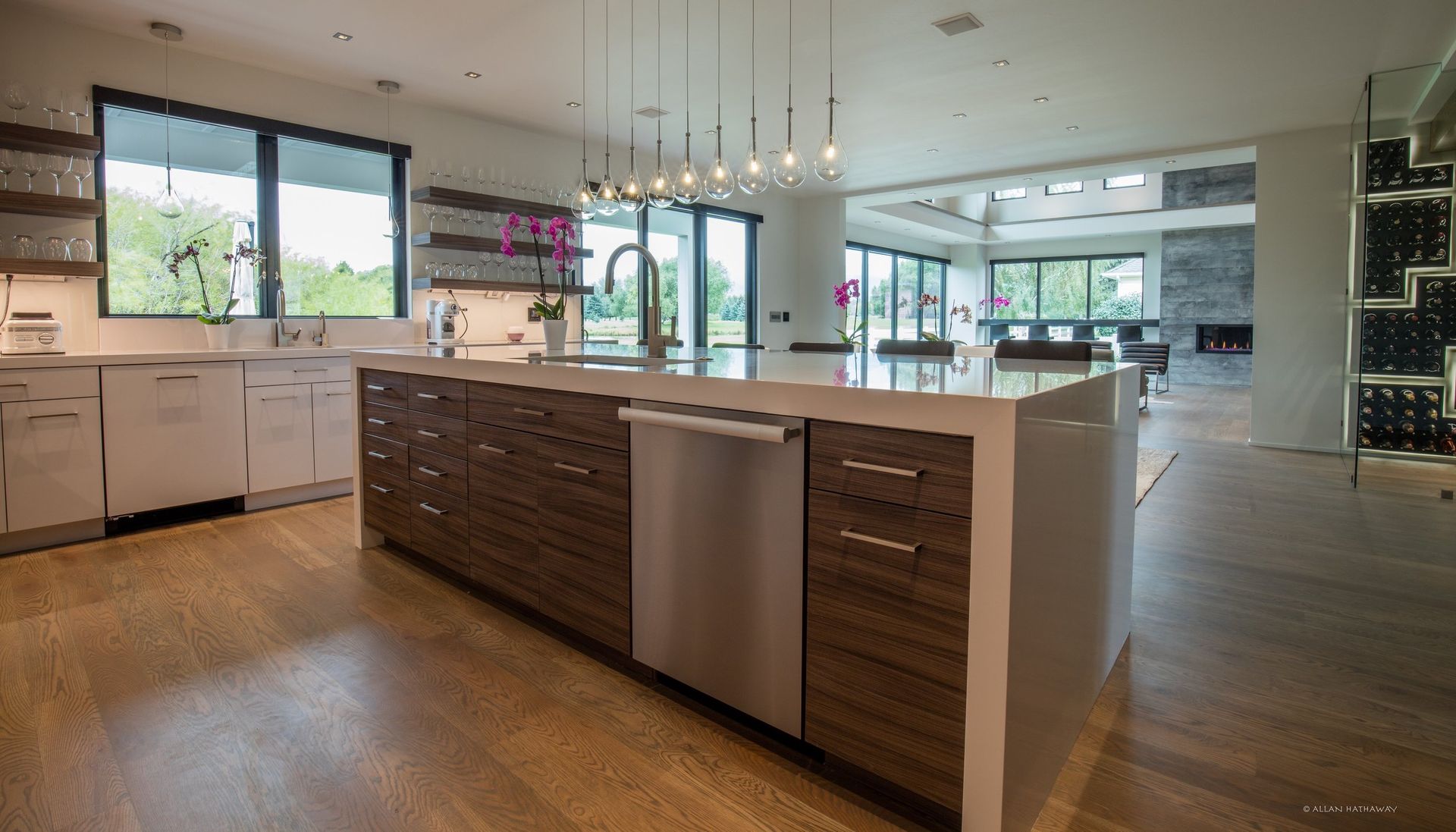 A modern, open-concept kitchen with a large wooden island, white countertops, stainless steel appliances, and wood floors.