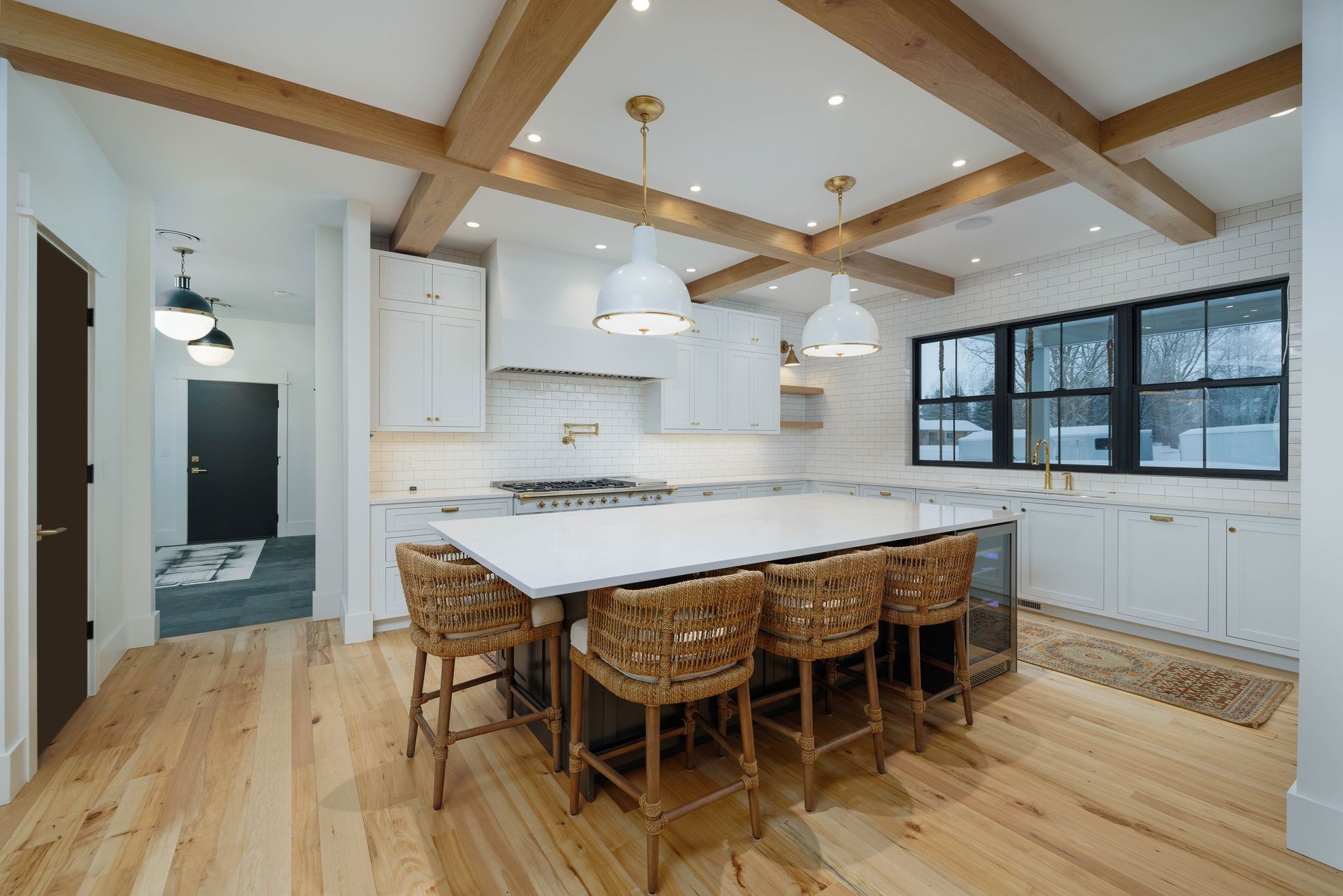 Bright modern kitchen featuring white cabinets, a large quartz island with four woven stools, and wooden ceiling beams.