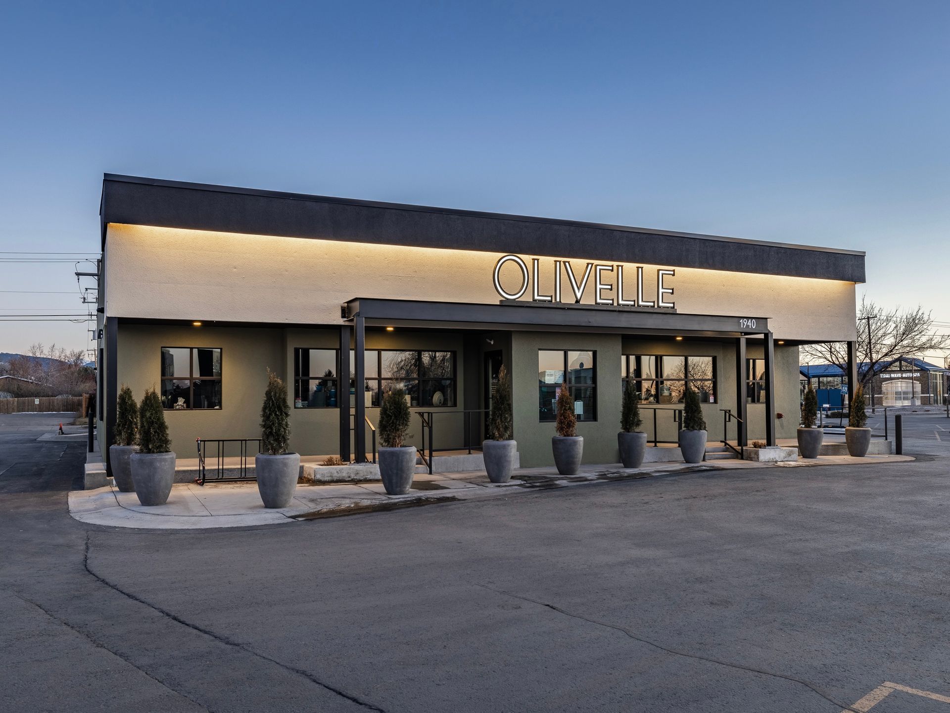 Modern storefront with “CHITEL” sign, lit facade, and potted plants at dusk