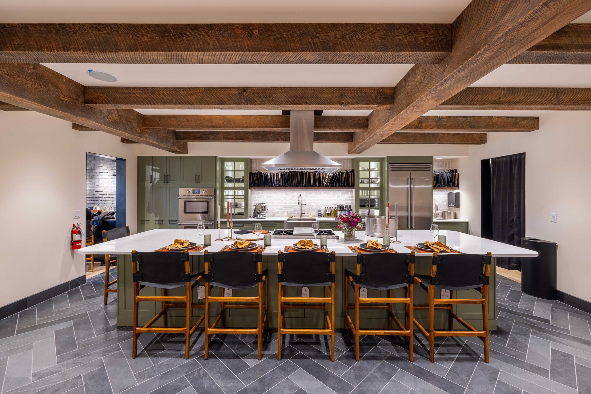 Modern kitchen with long island, black chairs, exposed wood beams, and gray tile flooring