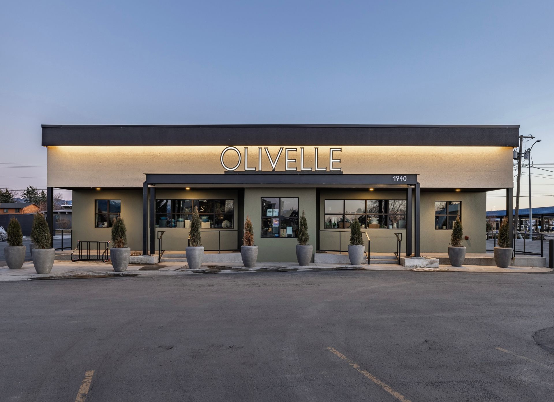 Front view of a storefront restaurant at dusk with lit signage and outdoor seating area