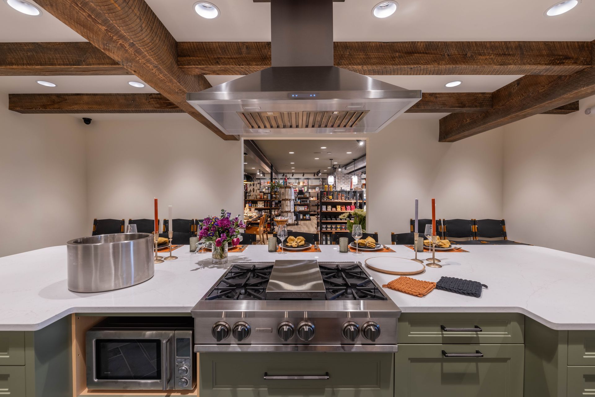 Modern kitchen island with stovetop, range hood, and candles overlooking a stocked market kitchen counter