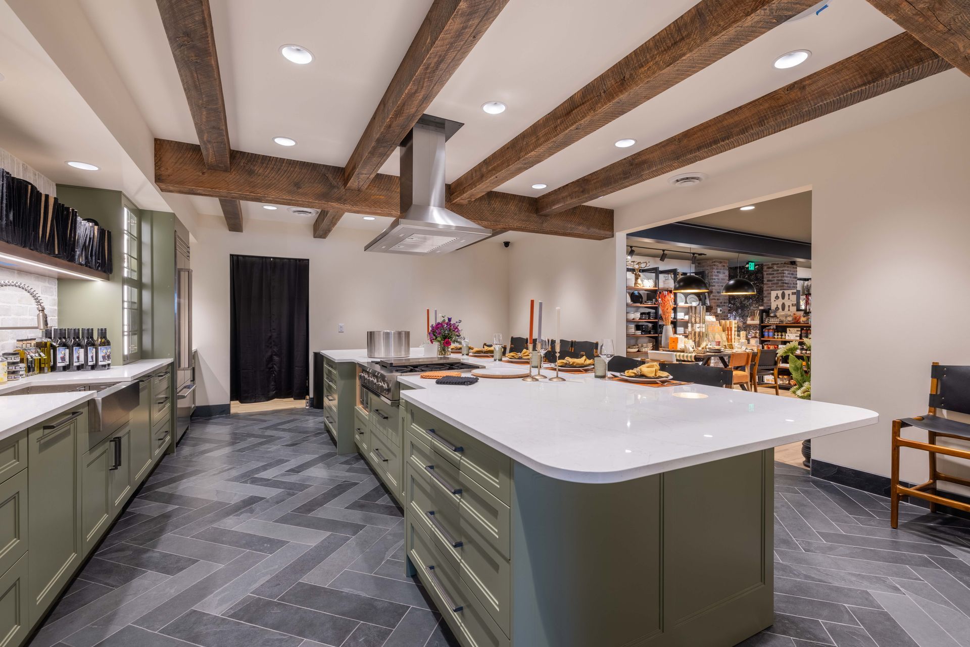 Modern kitchen with green island cabinets, white countertops, exposed wood beams, and a patterned gray floor