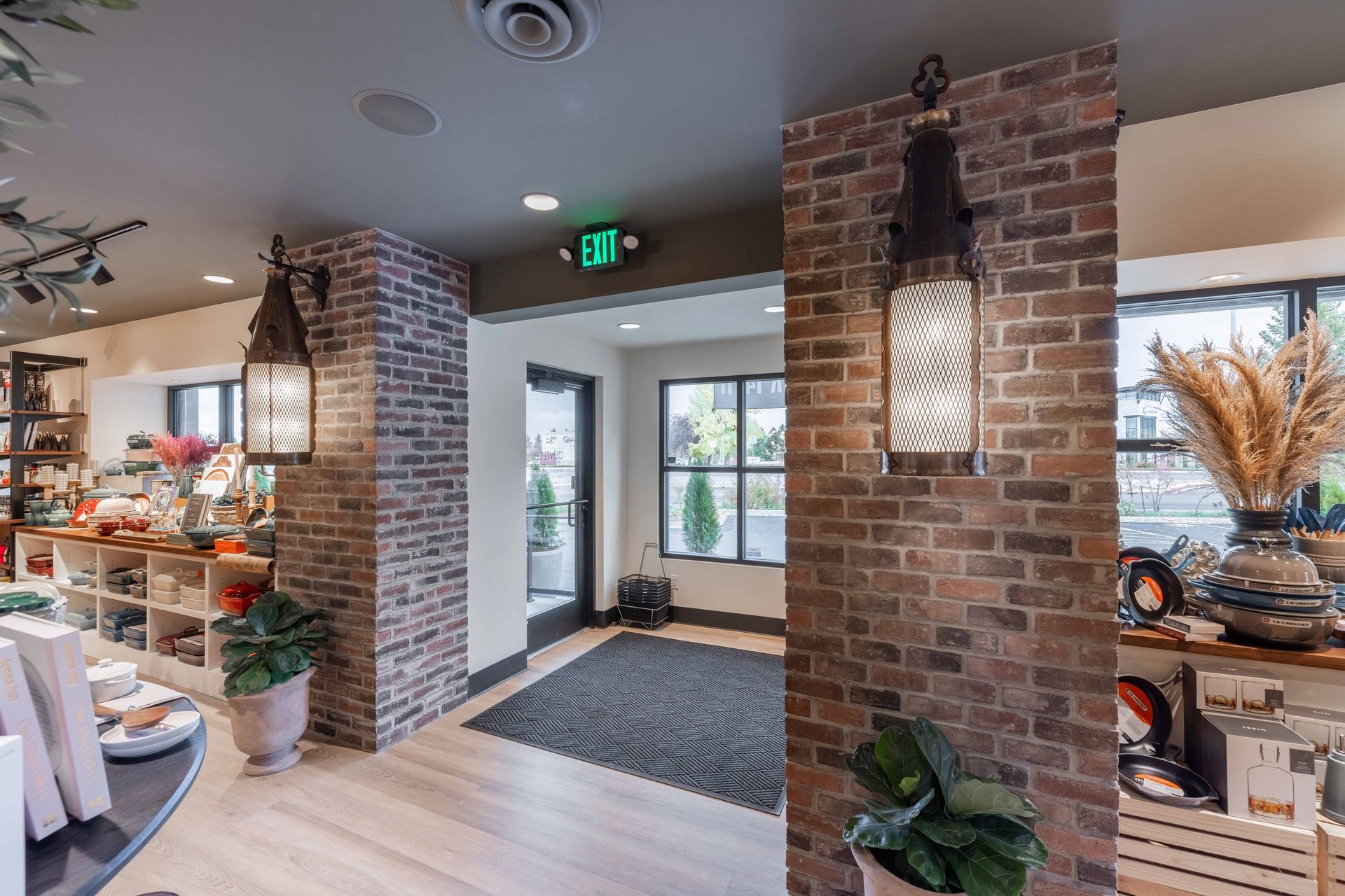 A well-lit store interior featuring exposed brick pillars, pendant lanterns, decorative items, and an exit door.