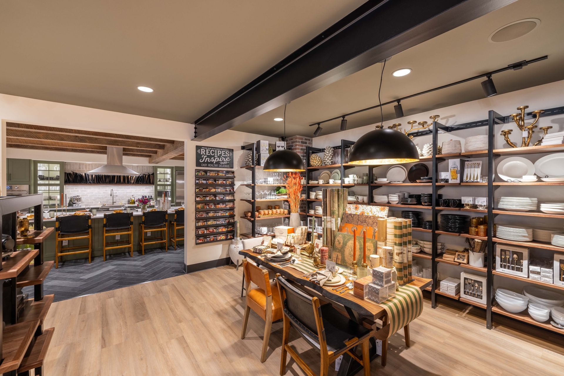 A modern home goods store featuring organized shelving with decor and a central dining display, with a kitchen in the back.