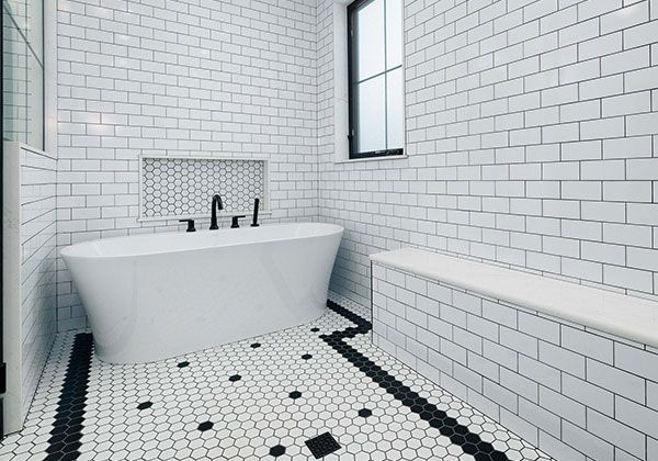 Modern white-tiled bathroom with freestanding tub, black-and-white mosaic floor, and bench seat.