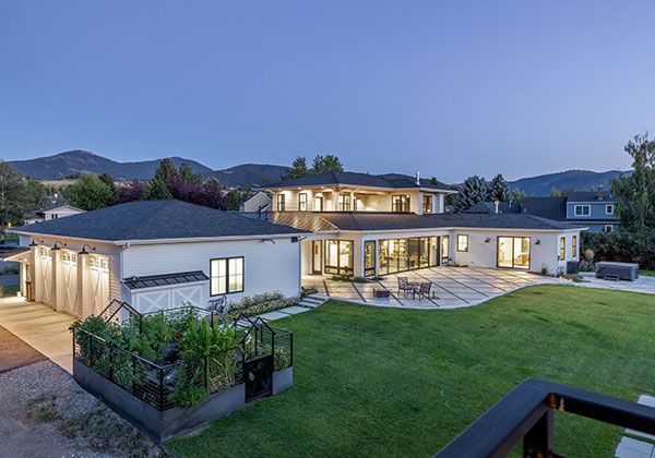 Modern two-story house with lit windows, patio, and large green lawn at dusk.