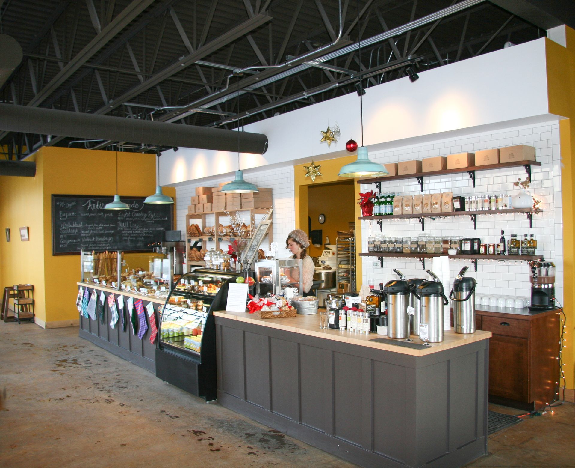 Coffee shop counter with espresso machines, mugs, and a barista under a high industrial ceiling