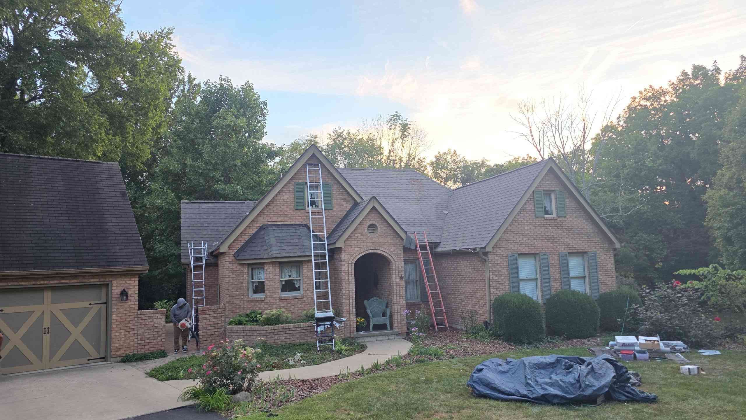 House with a brick facade and new roof, with ladders leaning against it. Garage on the left.