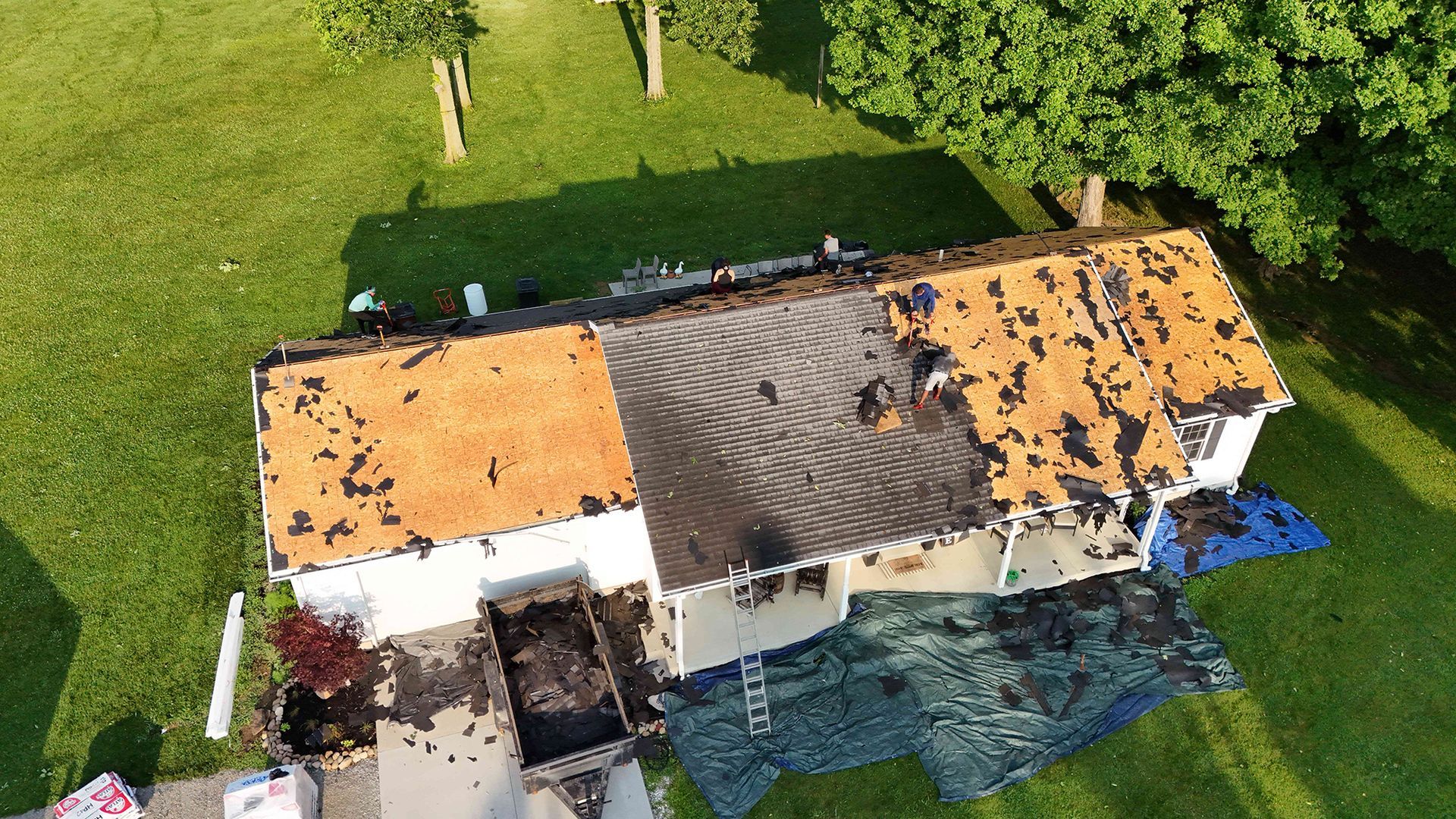 Aerial view of a house with damaged roof and tarps on the lawn.