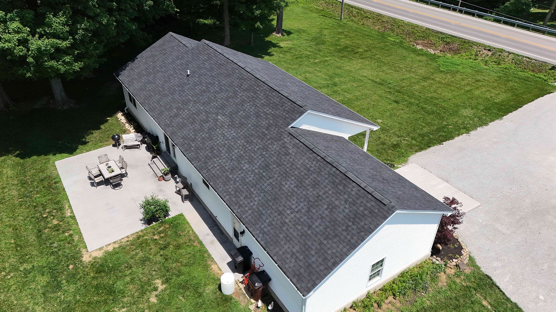Aerial view of a white building with a dark roof and surrounding green grass. Includes a patio and a driveway.