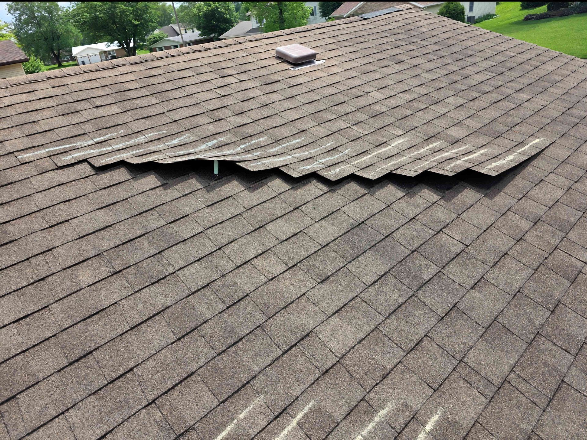 Brown asphalt shingle roof with a section of shingles buckling upwards, likely due to damage.