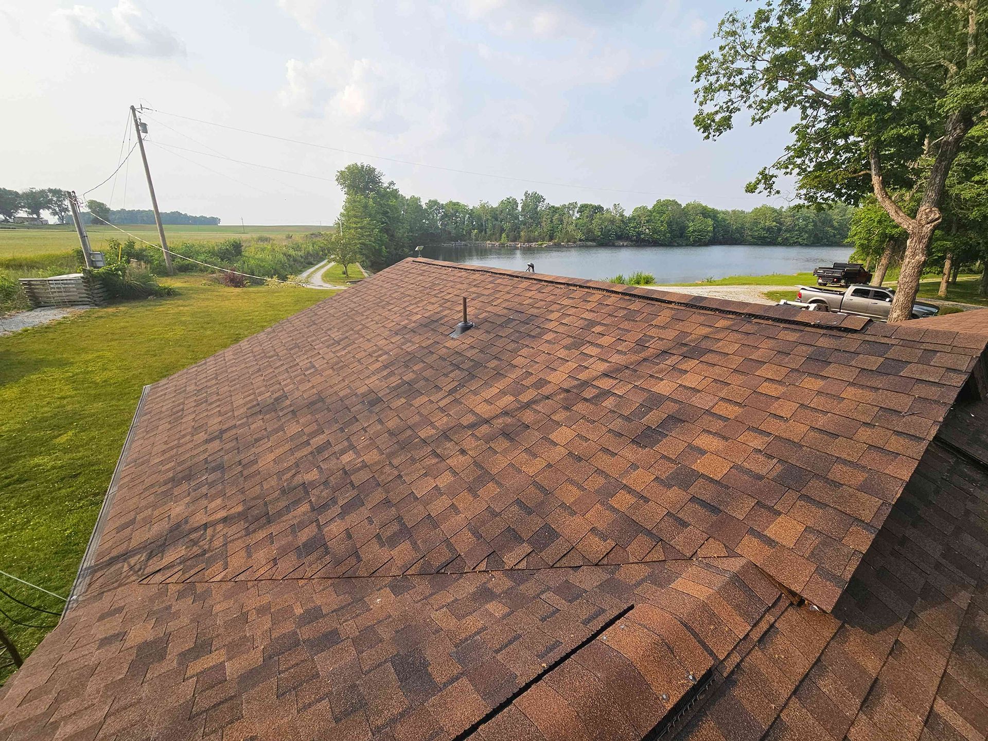 Brown shingled roof with a scenic lake and green field in the background on a sunny day.