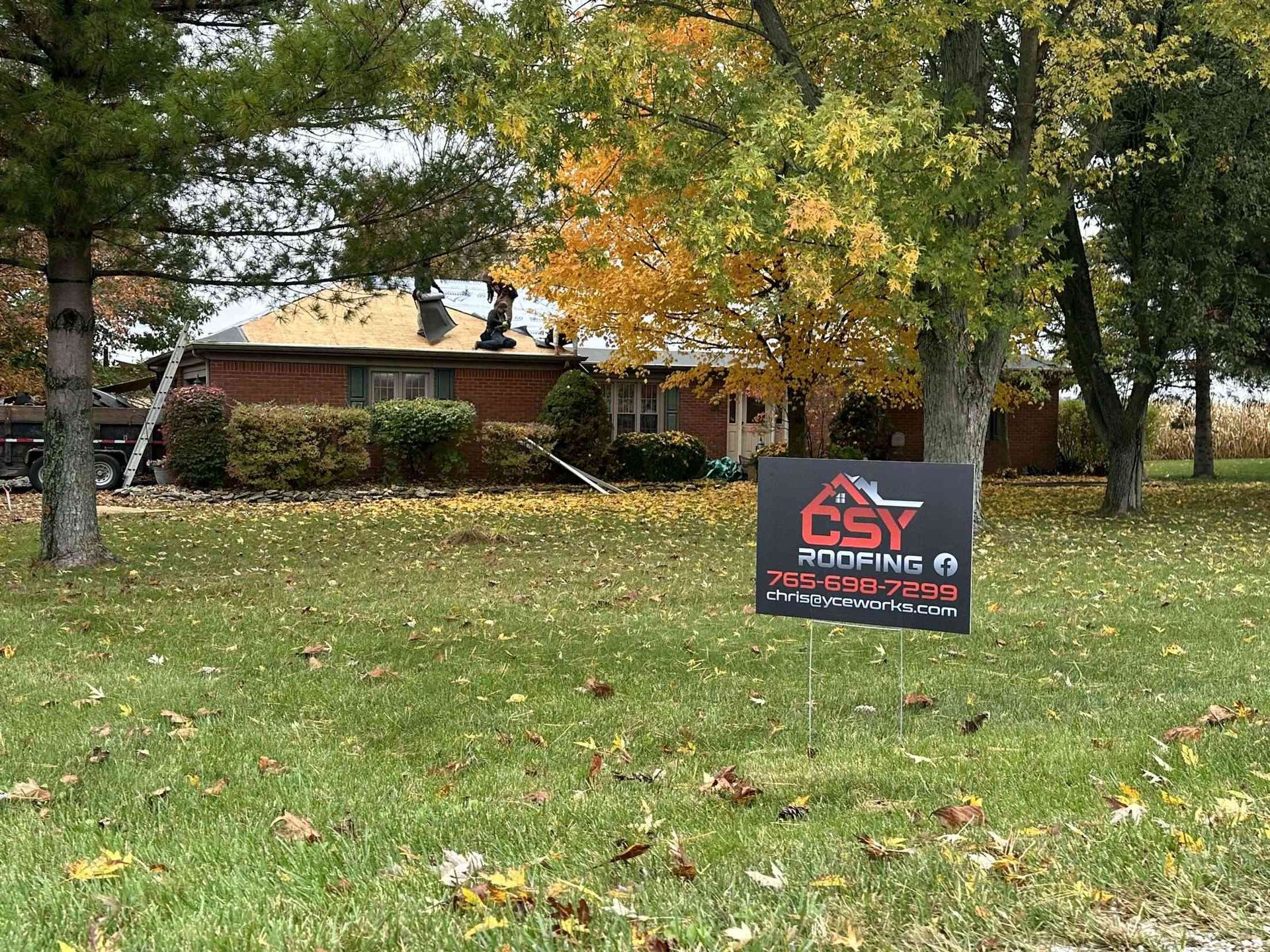 A residential roof being worked on by roofers; a CSY Roofing sign in the foreground.