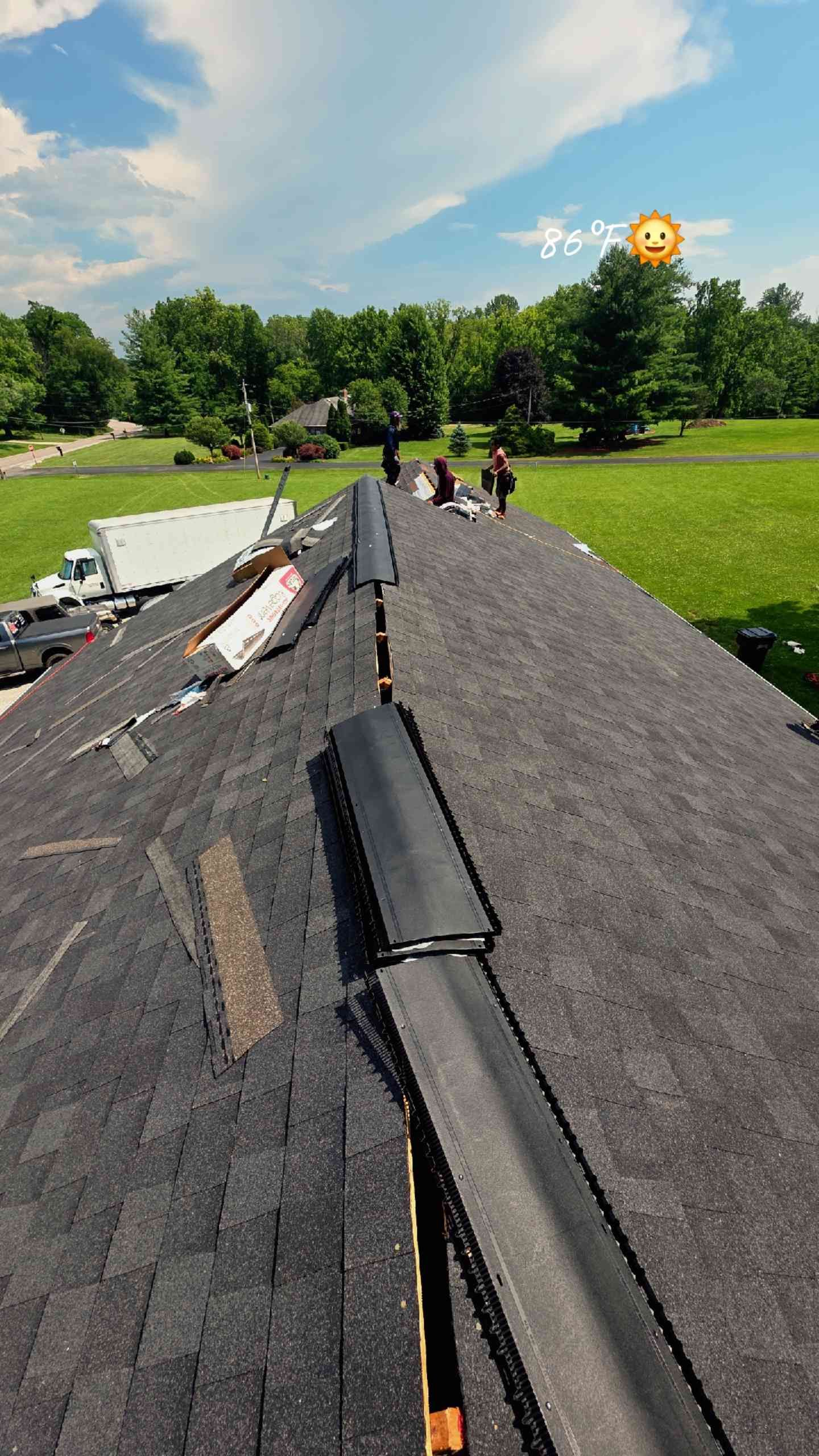 Workers installing shingles on a roof on a sunny day.