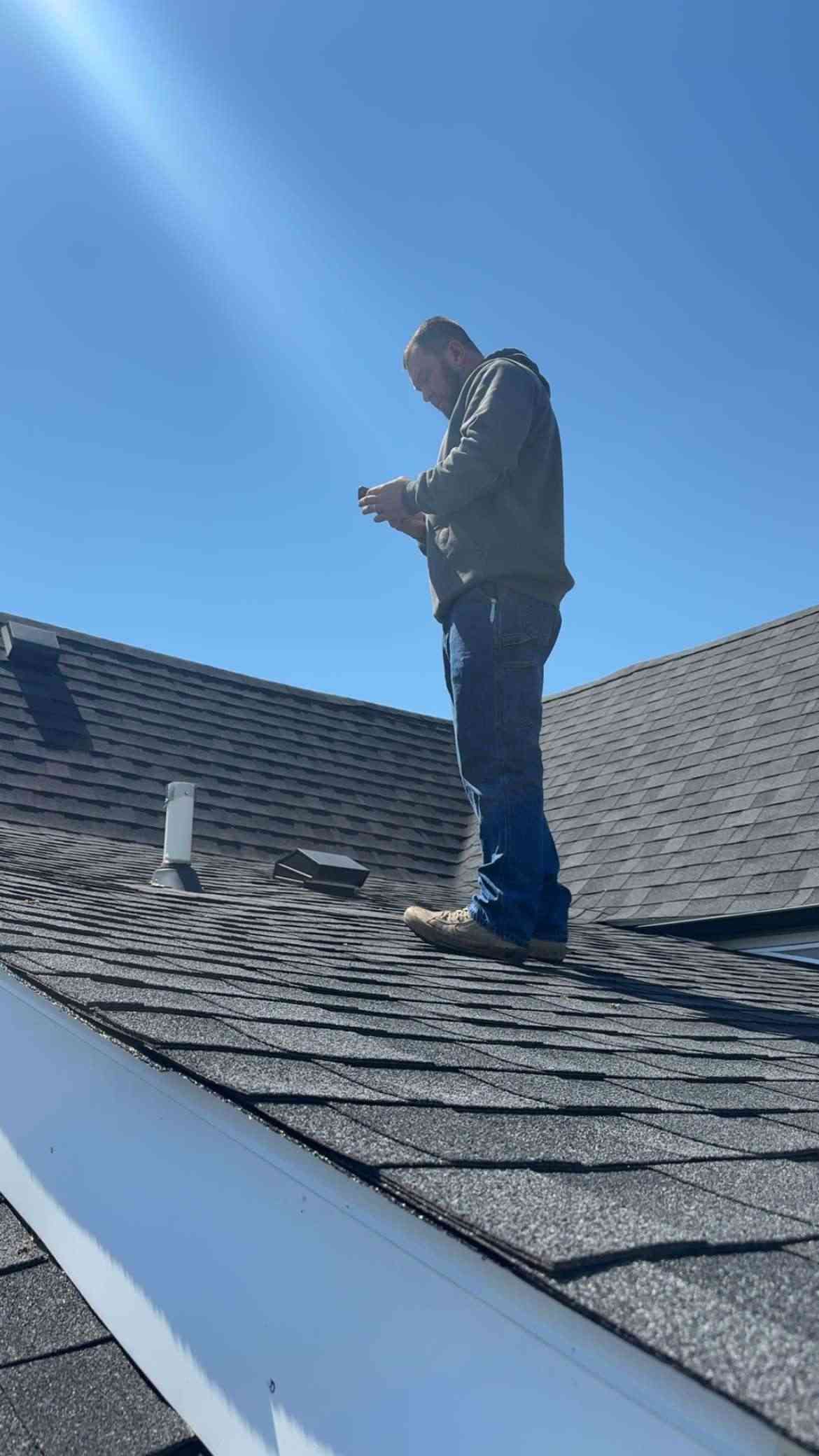 Man standing on a rooftop, holding a phone, on a sunny day.