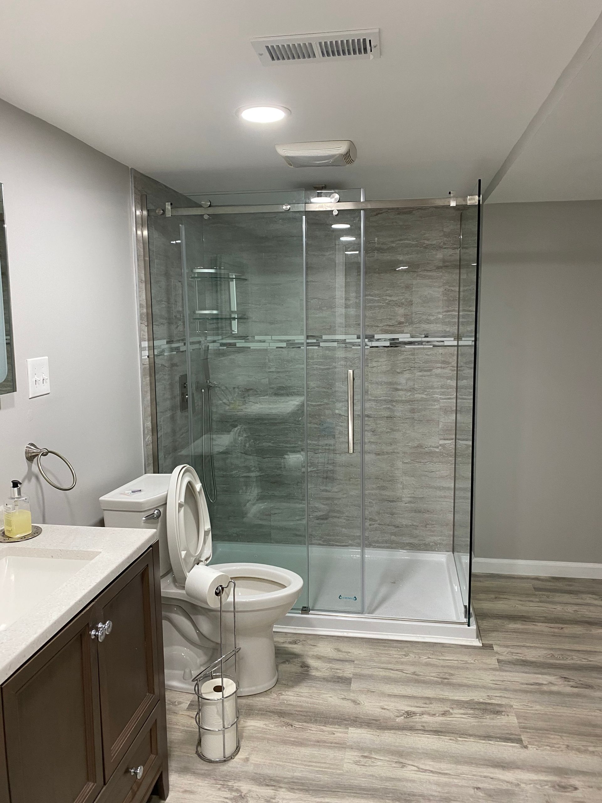Bathroom with glass shower enclosure, toilet, vanity sink, and wood-look flooring.