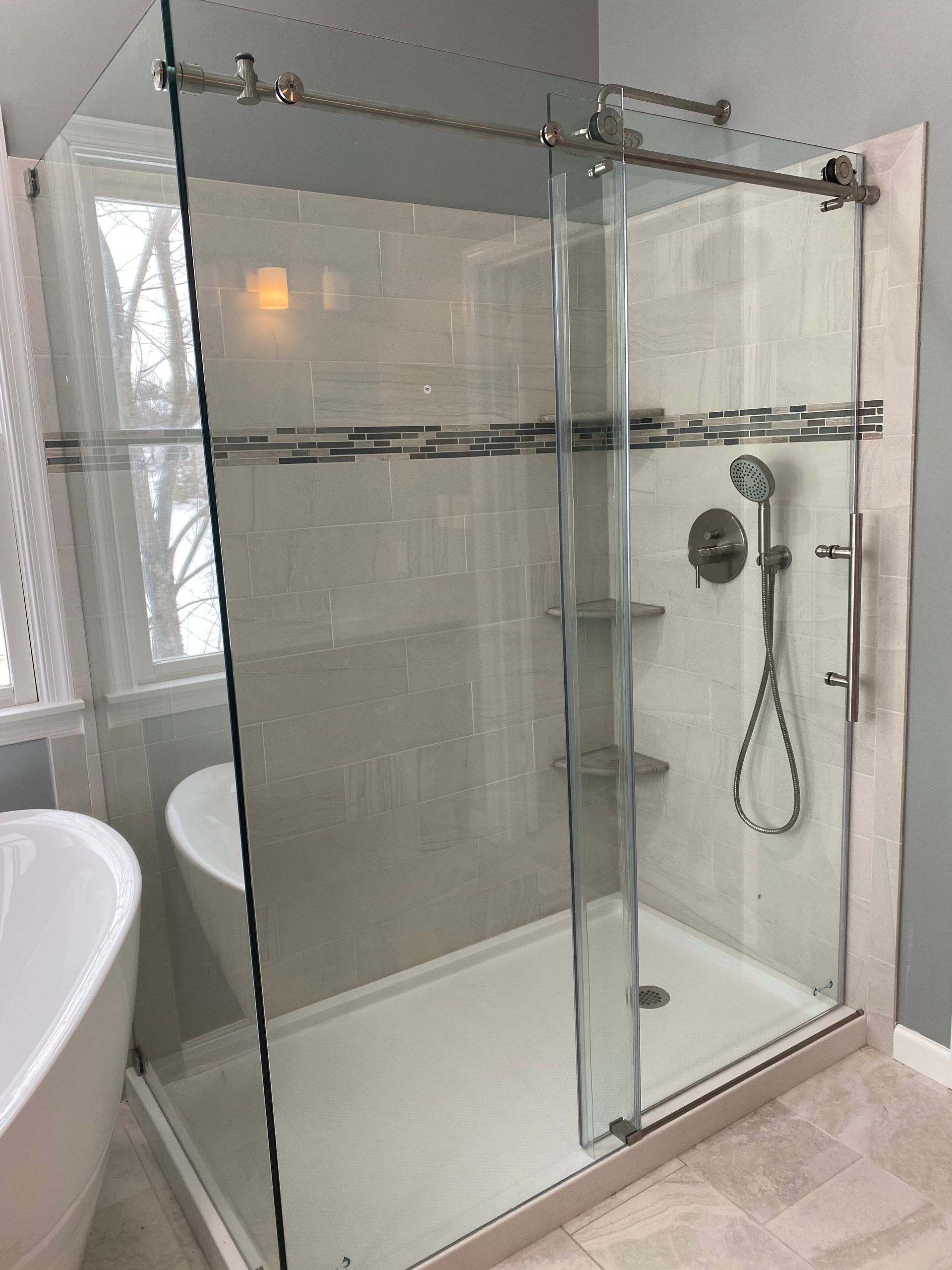 Glass walk-in shower with sliding door and chrome fixtures in a bright bathroom