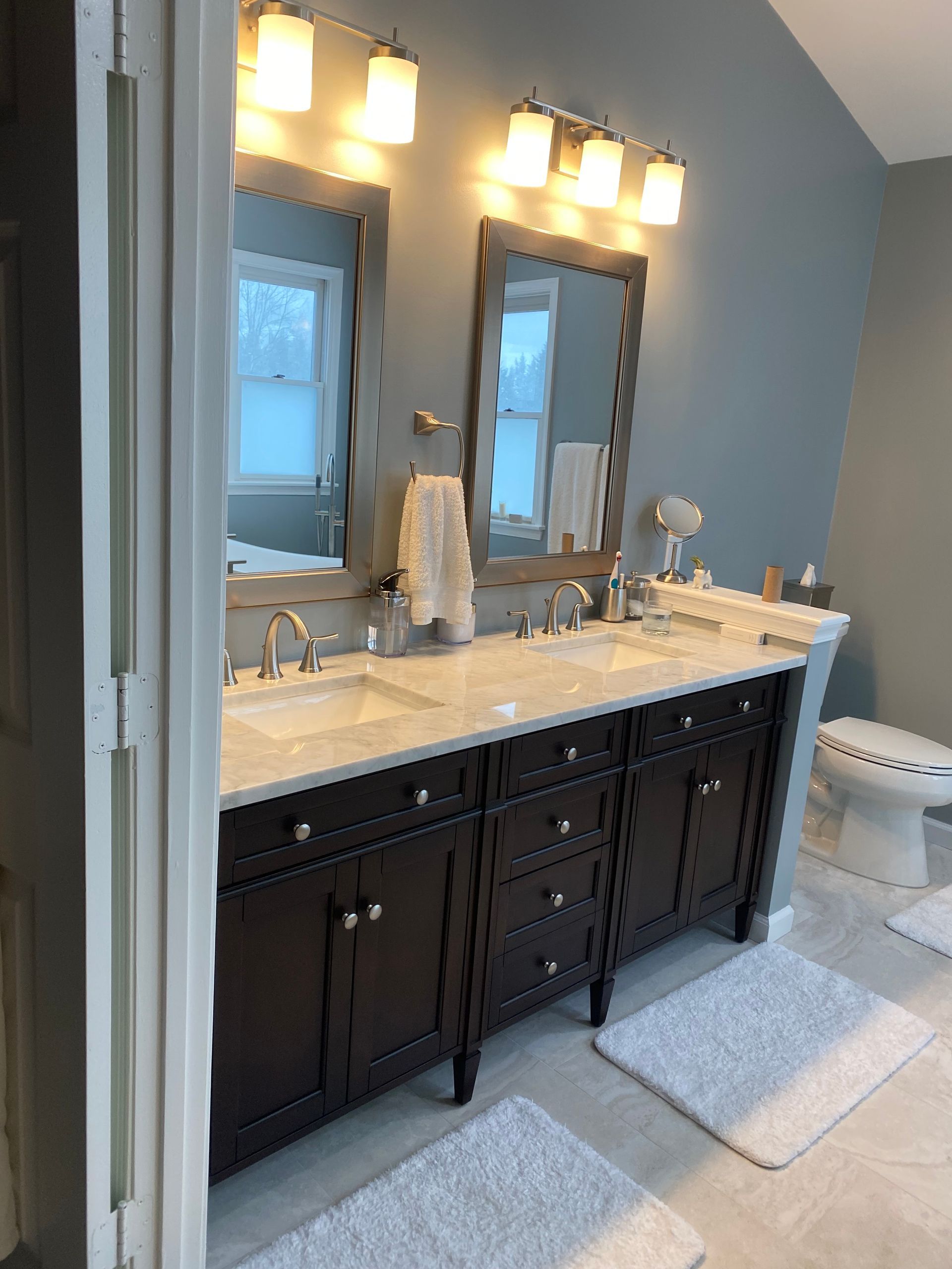 Double sink bathroom vanity with dark cabinets, marble countertop, and large mirror under wall sconces