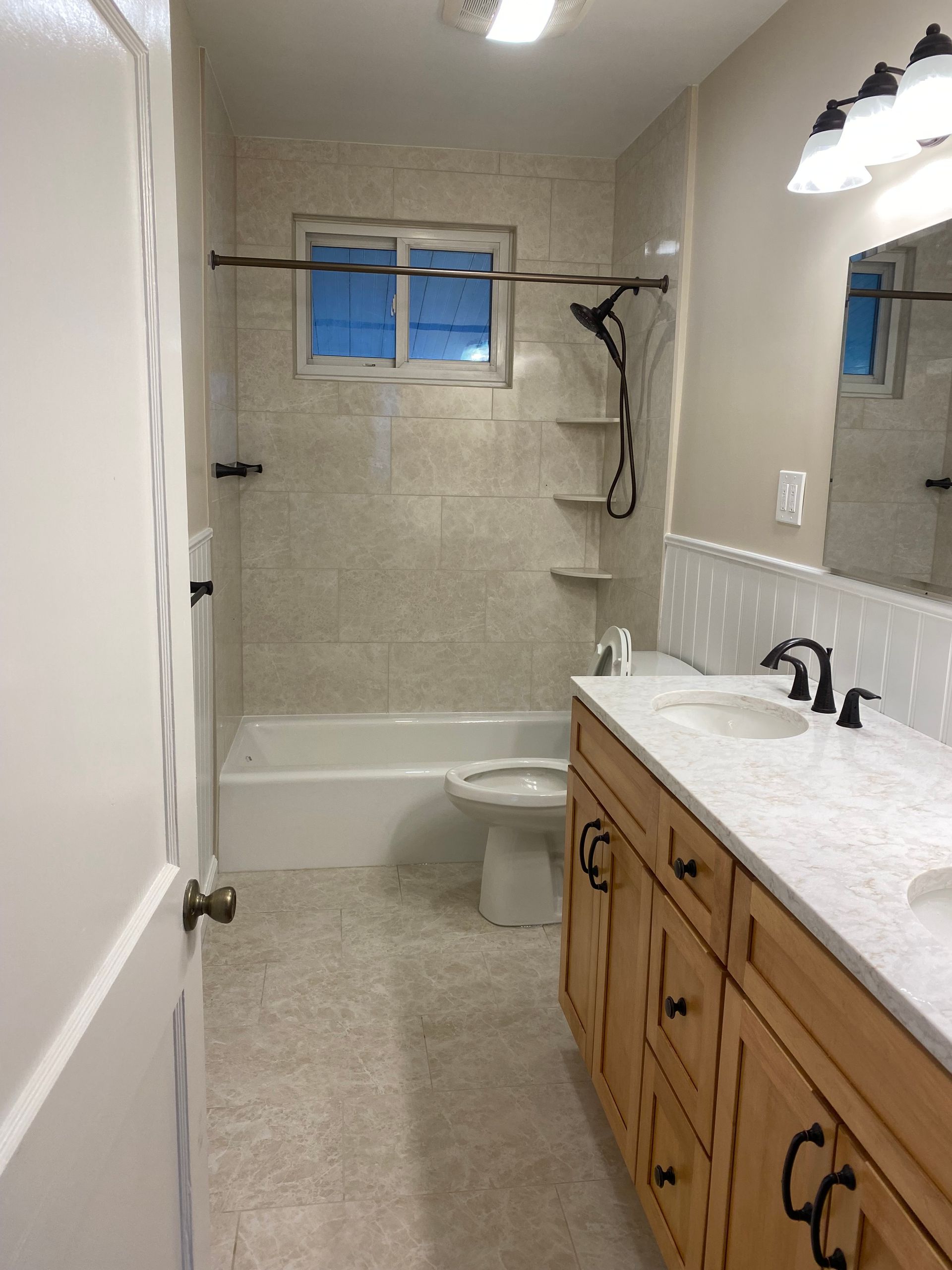Bathroom with tub, shower, vanity, and window, shown in neutral tones.