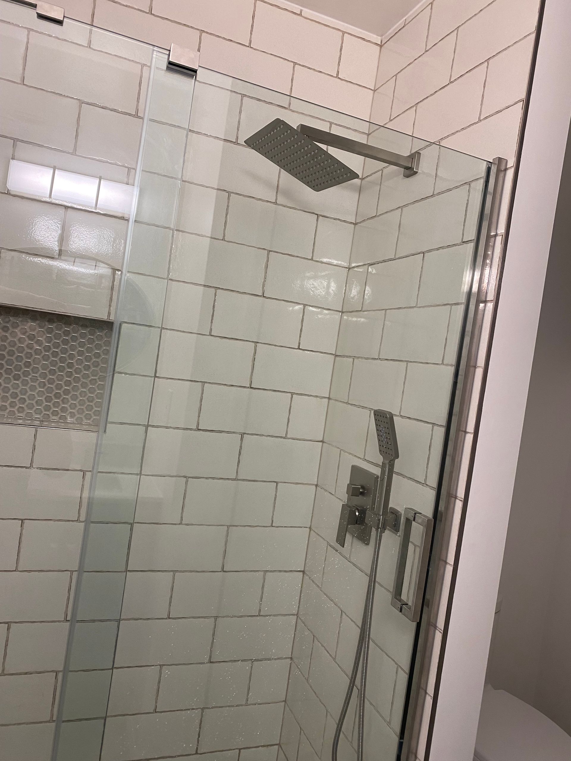 Tiled shower stall with glass door and chrome showerhead.