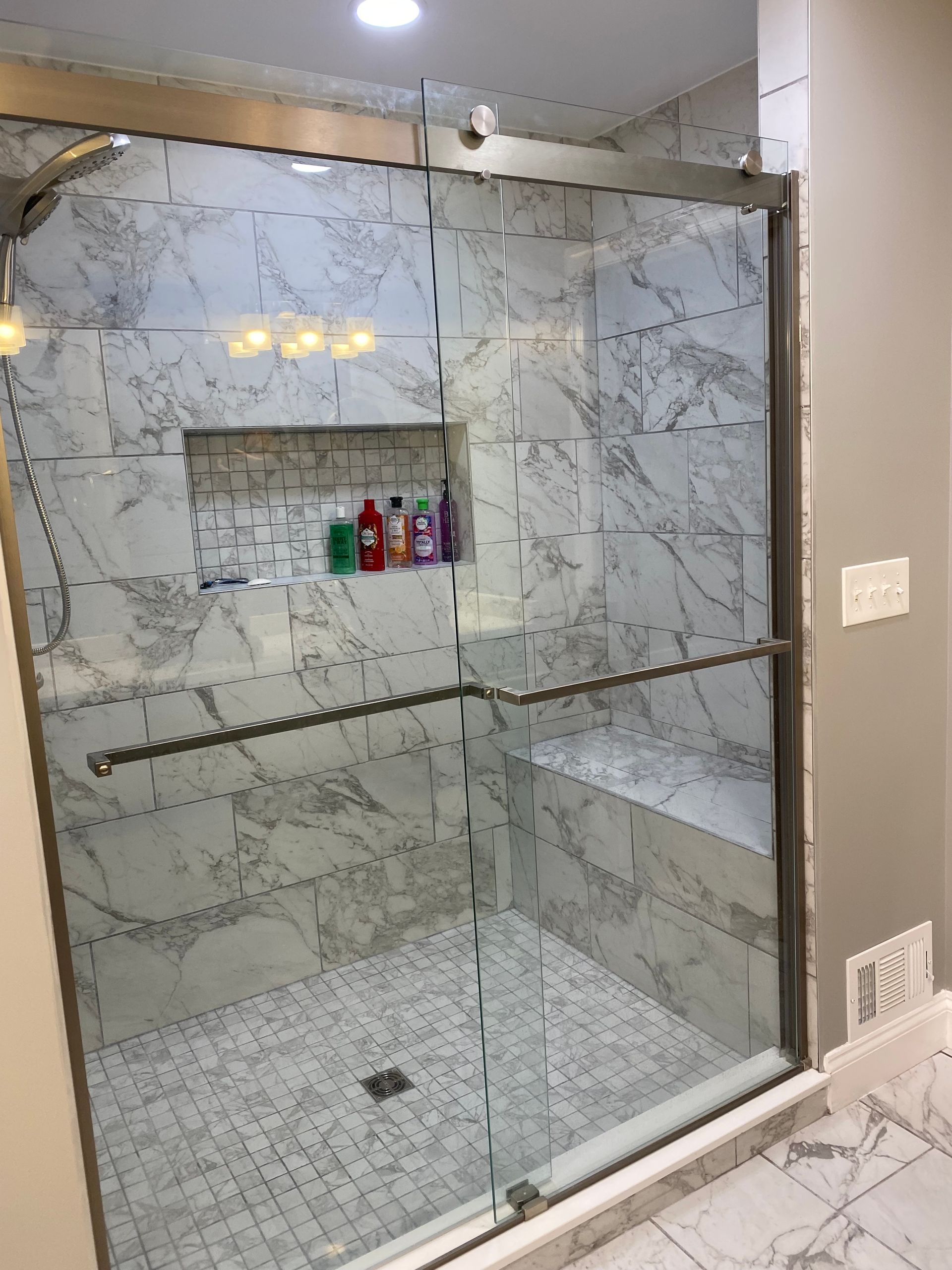 Modern tiled shower with glass sliding door, built-in shelf holding toiletries, and gray walls.
