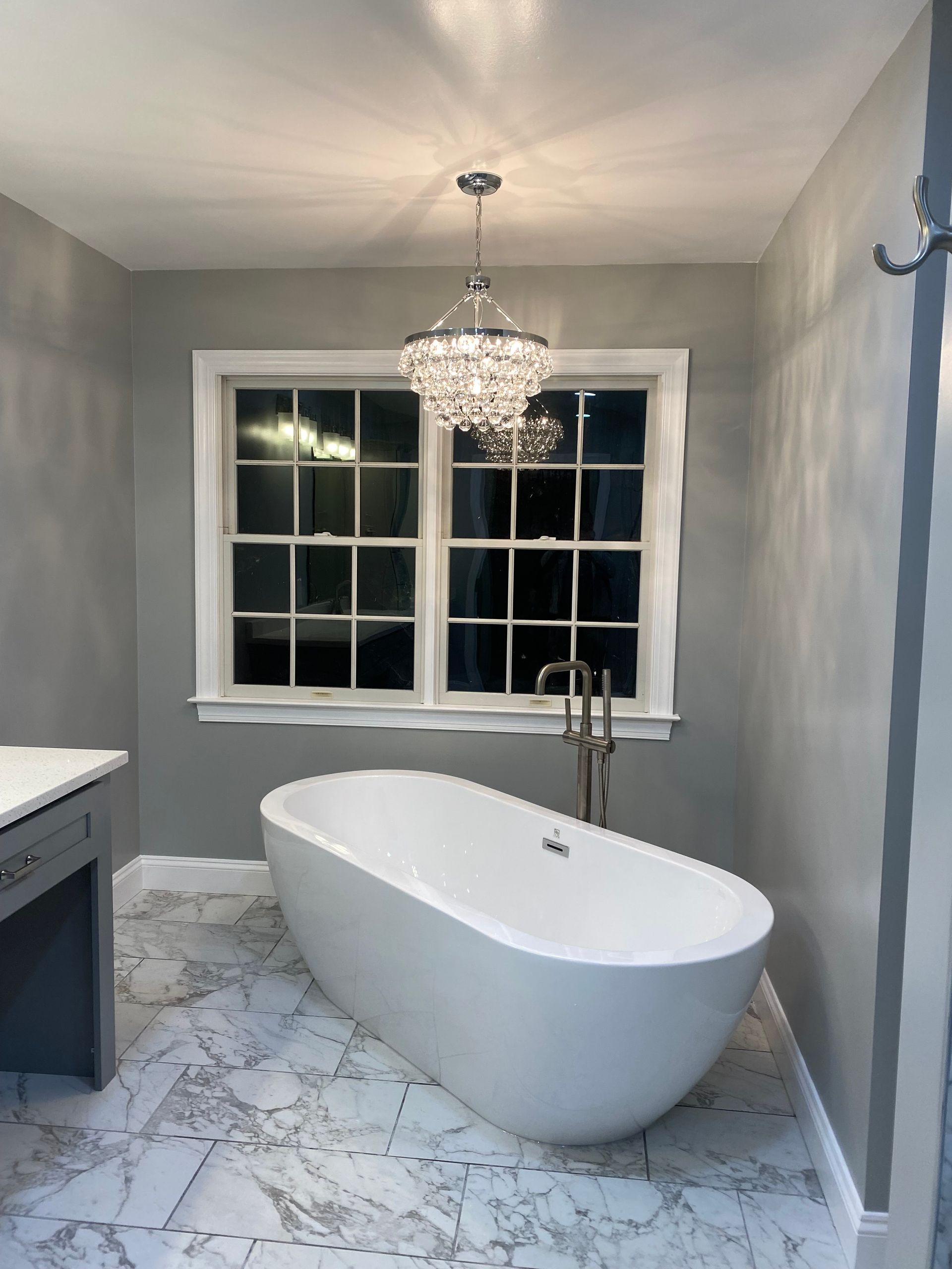 Modern bathroom with freestanding tub, chandelier, gray walls, and marble floor