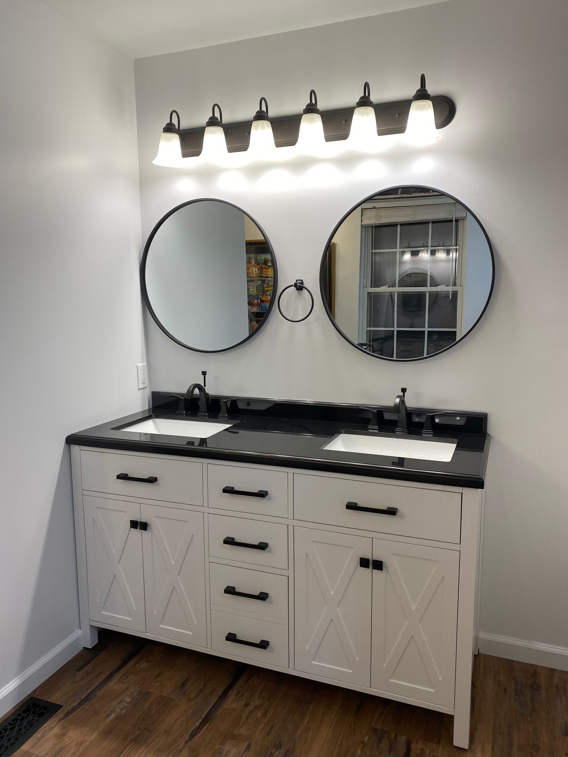 Modern double vanity with black countertop, round mirrors, and five-light wall fixture in a white bathroom.