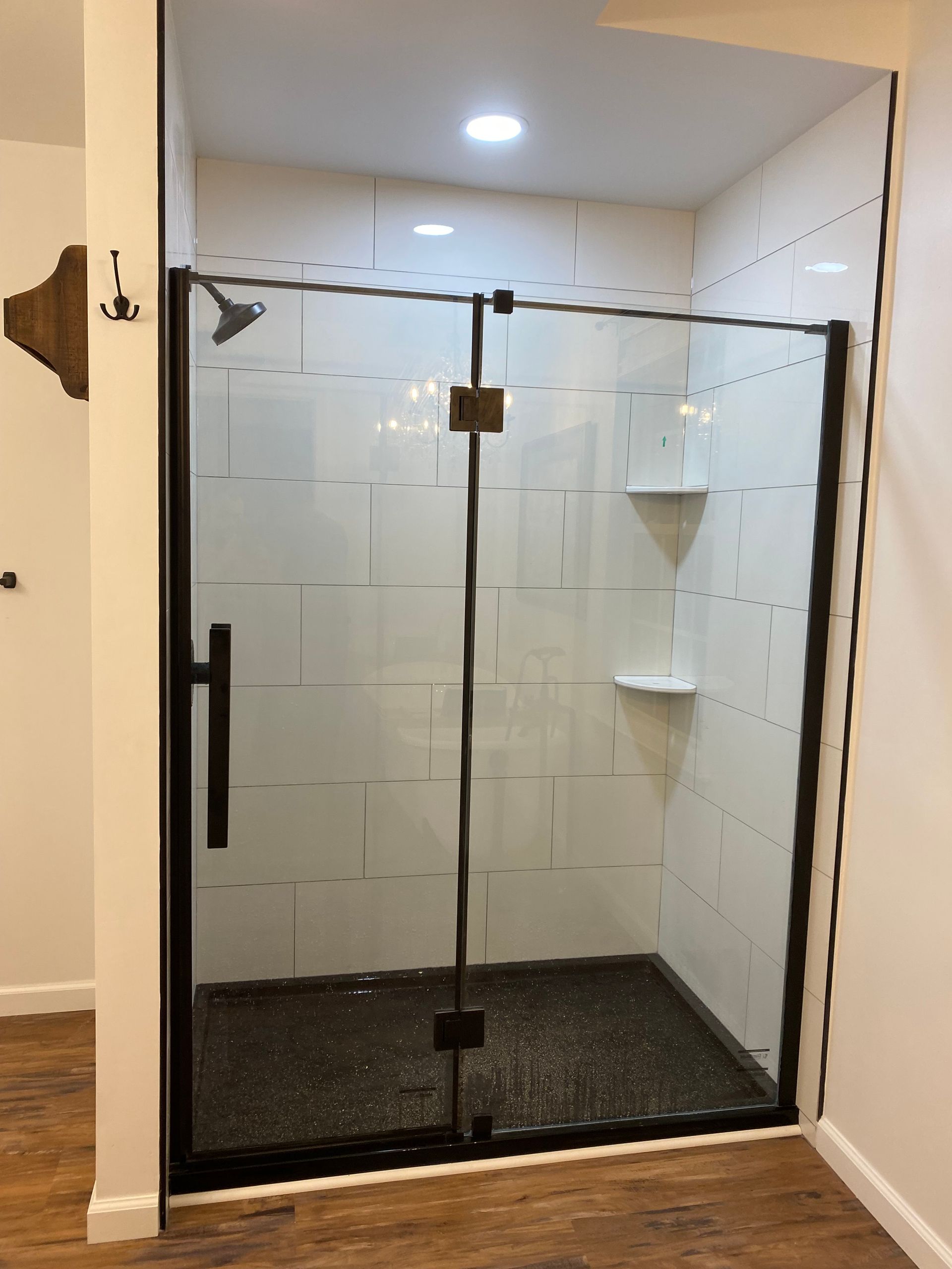 Glass-enclosed shower with black-framed doors and white tiled walls in a bathroom