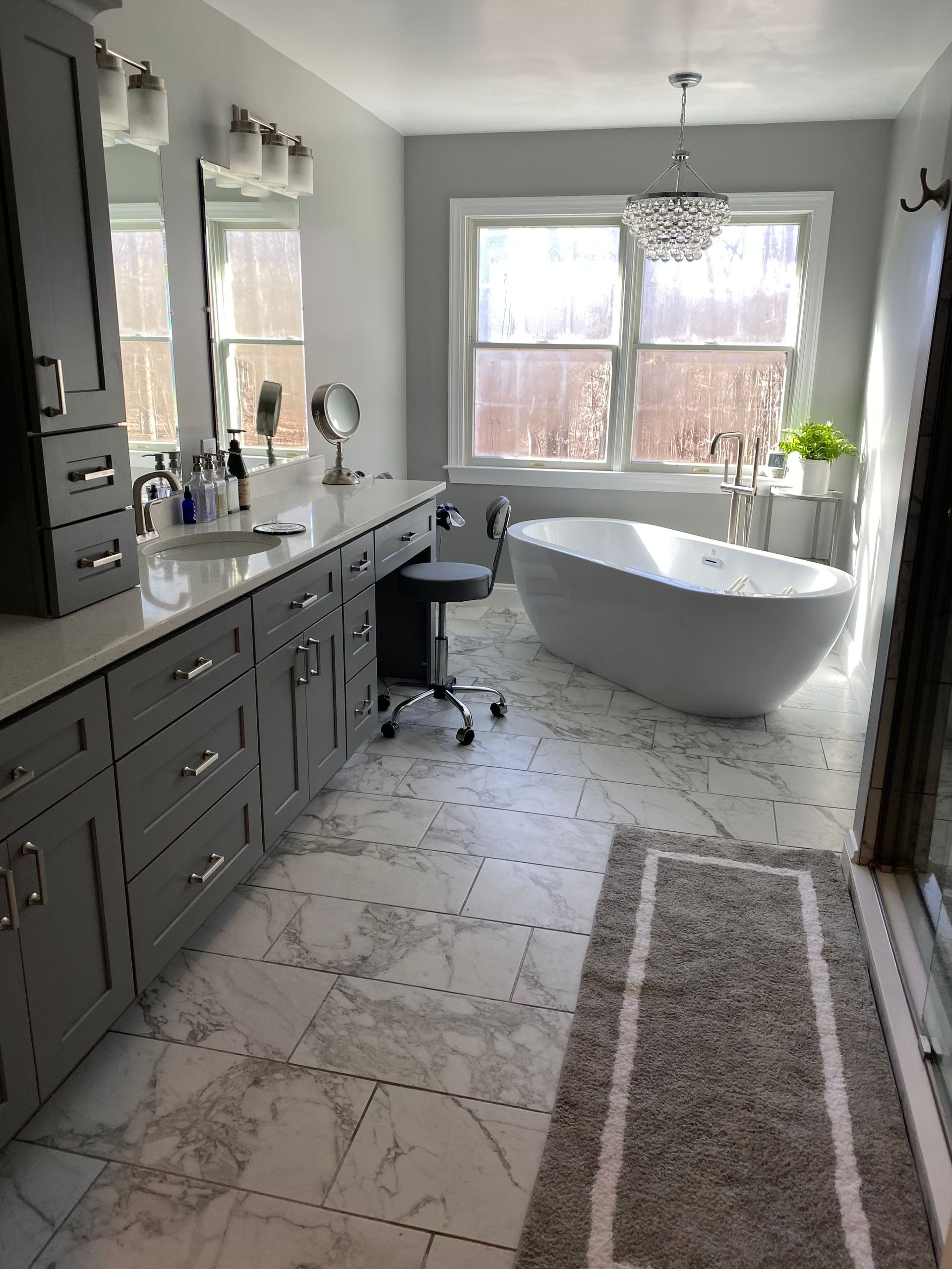 Bright bathroom with dark vanity, freestanding tub, and large window overlooking snowy trees.