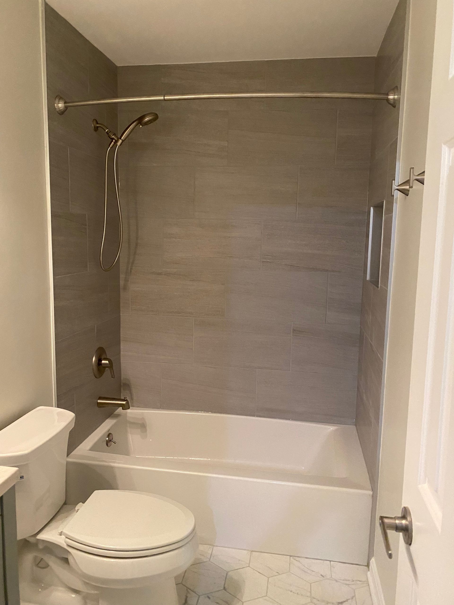 Small bathroom with tub-shower, toilet, and gray tile wall.