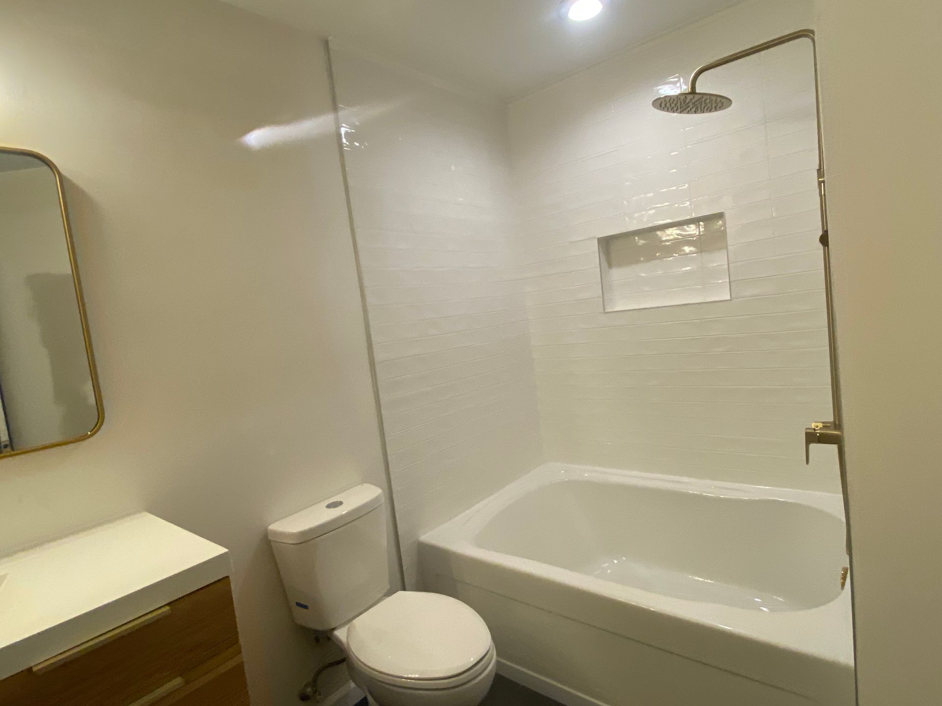 Bright bathroom with toilet, bathtub, shower, sink, and mirror on white tiled walls