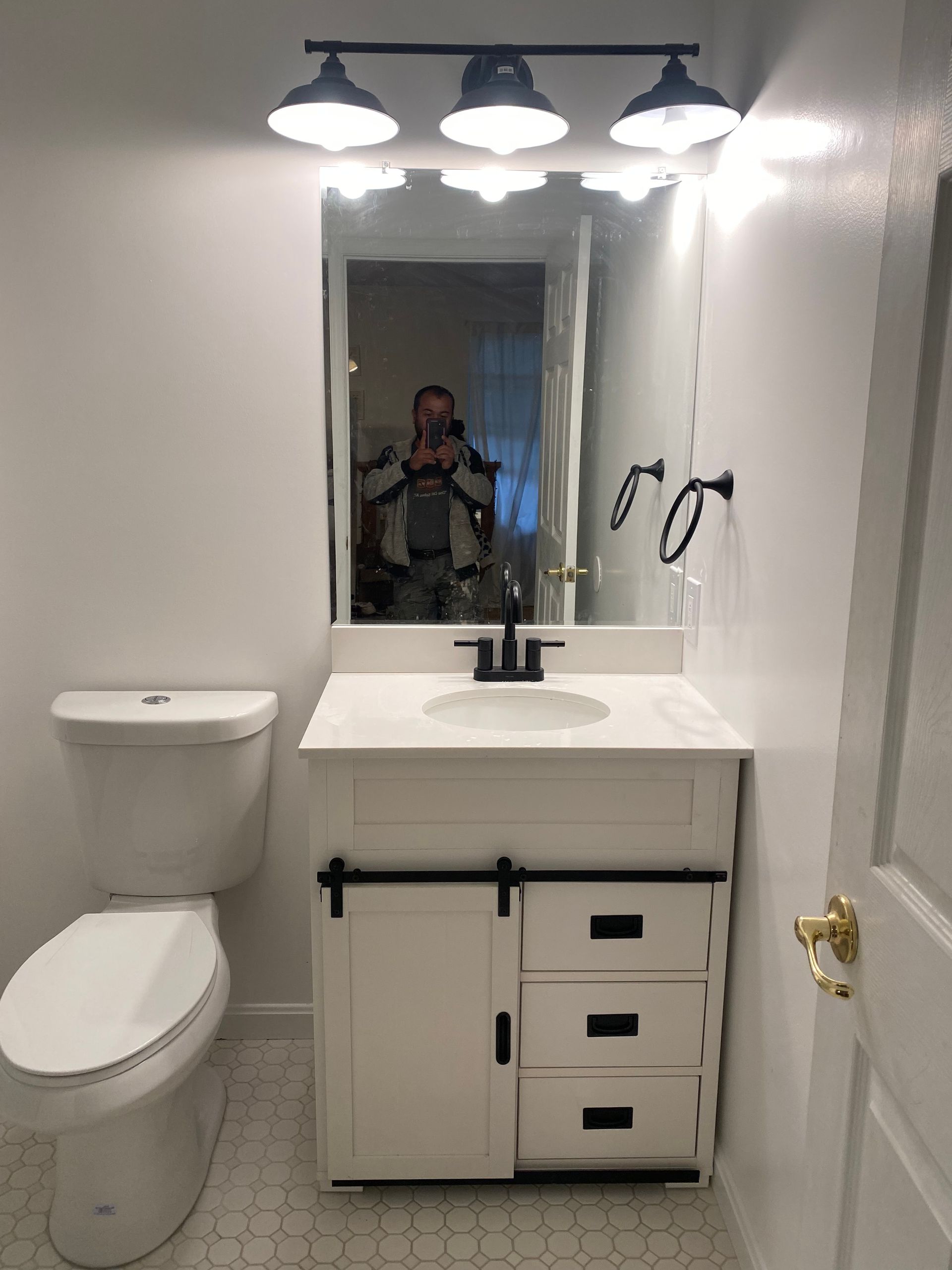 Small bathroom with white vanity, toilet, mirror, and three-light fixture.