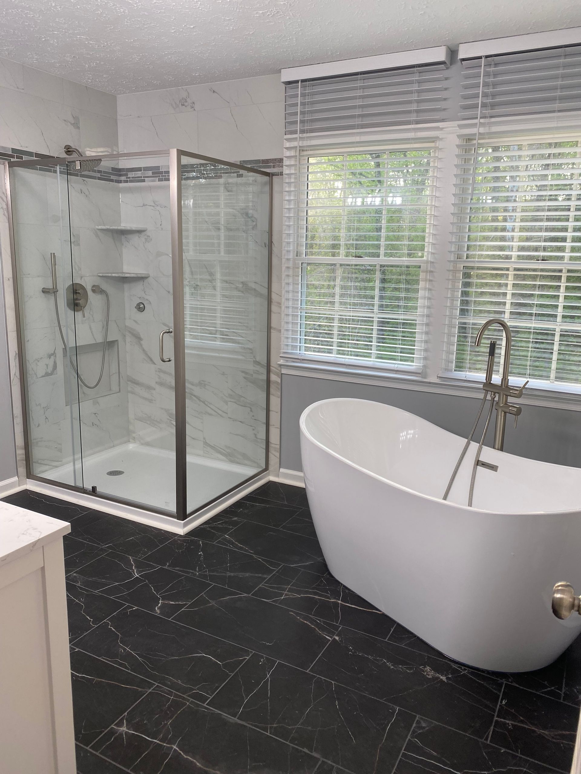 Modern bathroom with glass shower, freestanding tub, and window blinds