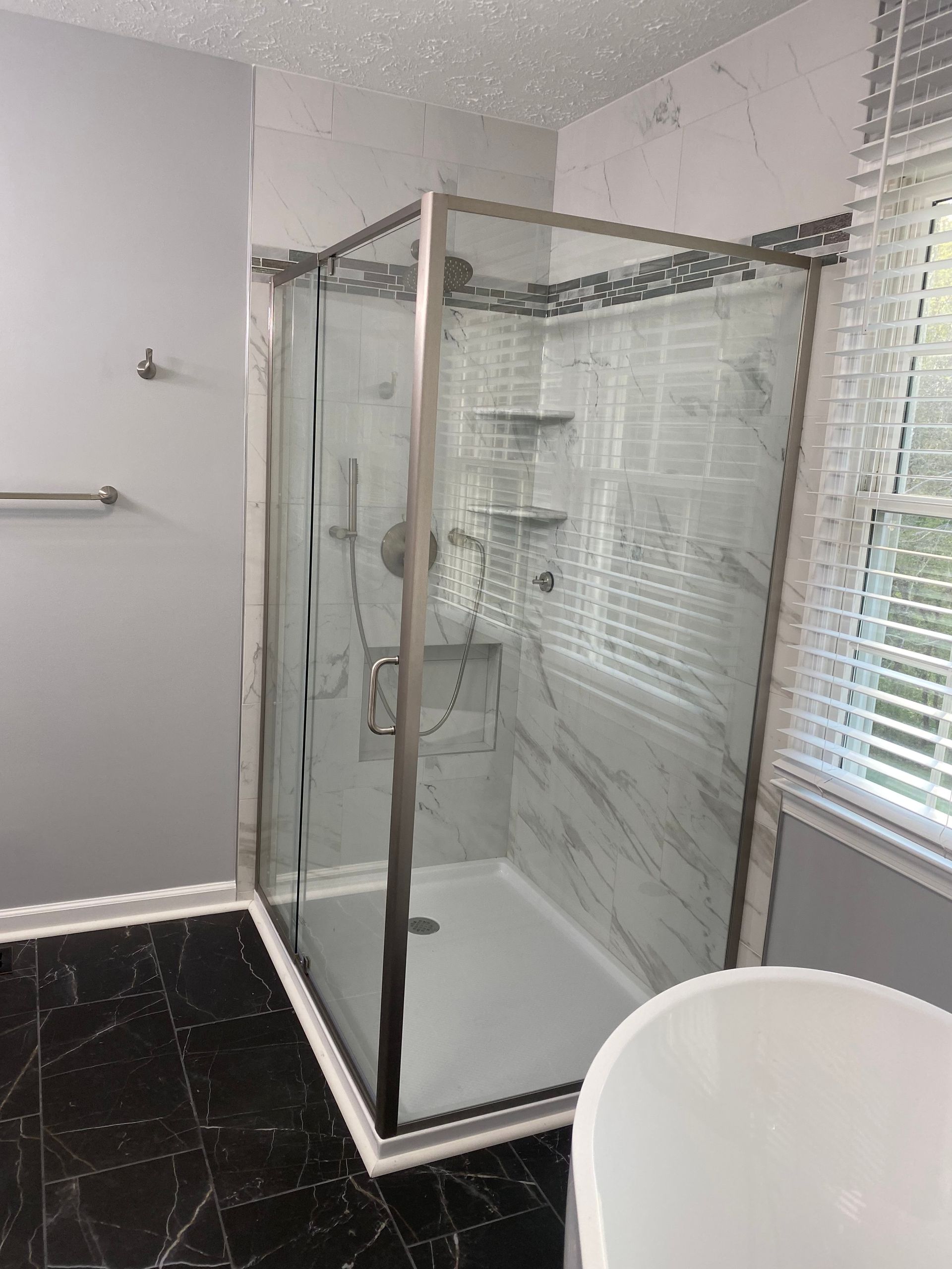 Modern bathroom with a glass walk-in shower, white tub, and black tile floor