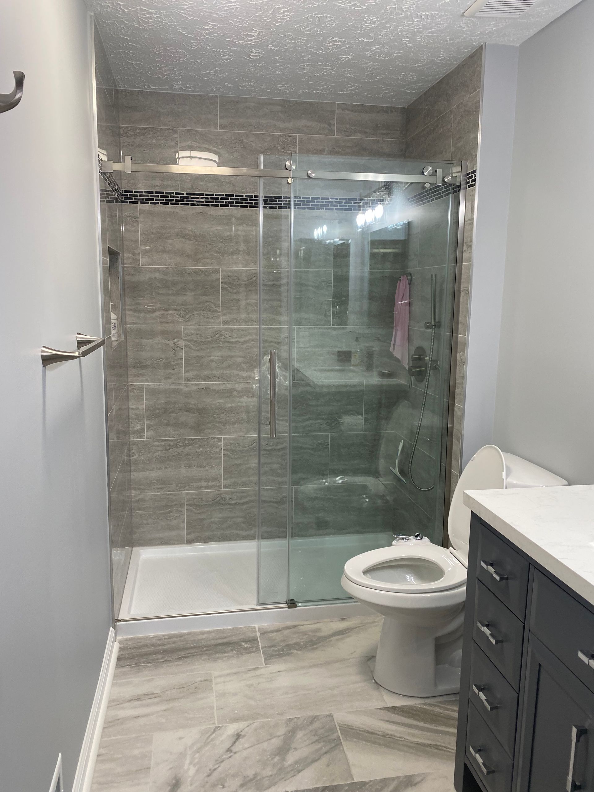 Small modern bathroom with a glass shower, toilet, gray walls, and vanity cabinets