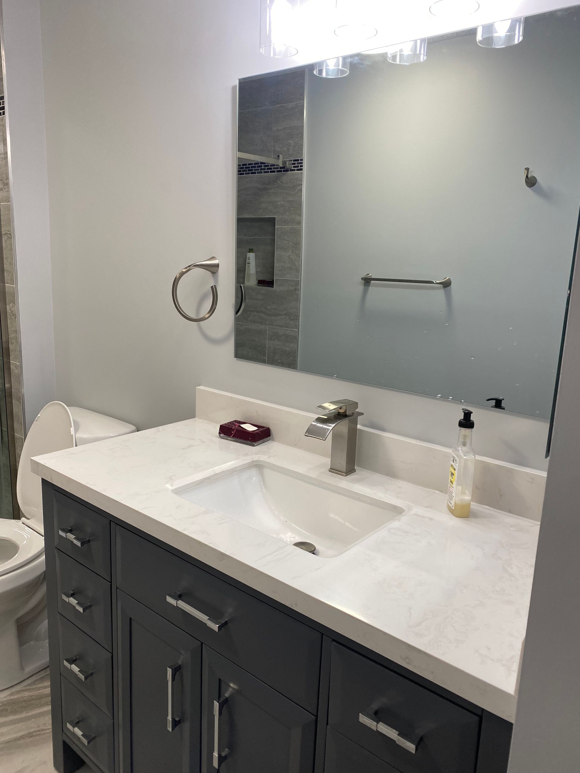 Bathroom vanity with white countertop, dark gray cabinets, mirror, sink, and wall sconce lighting.