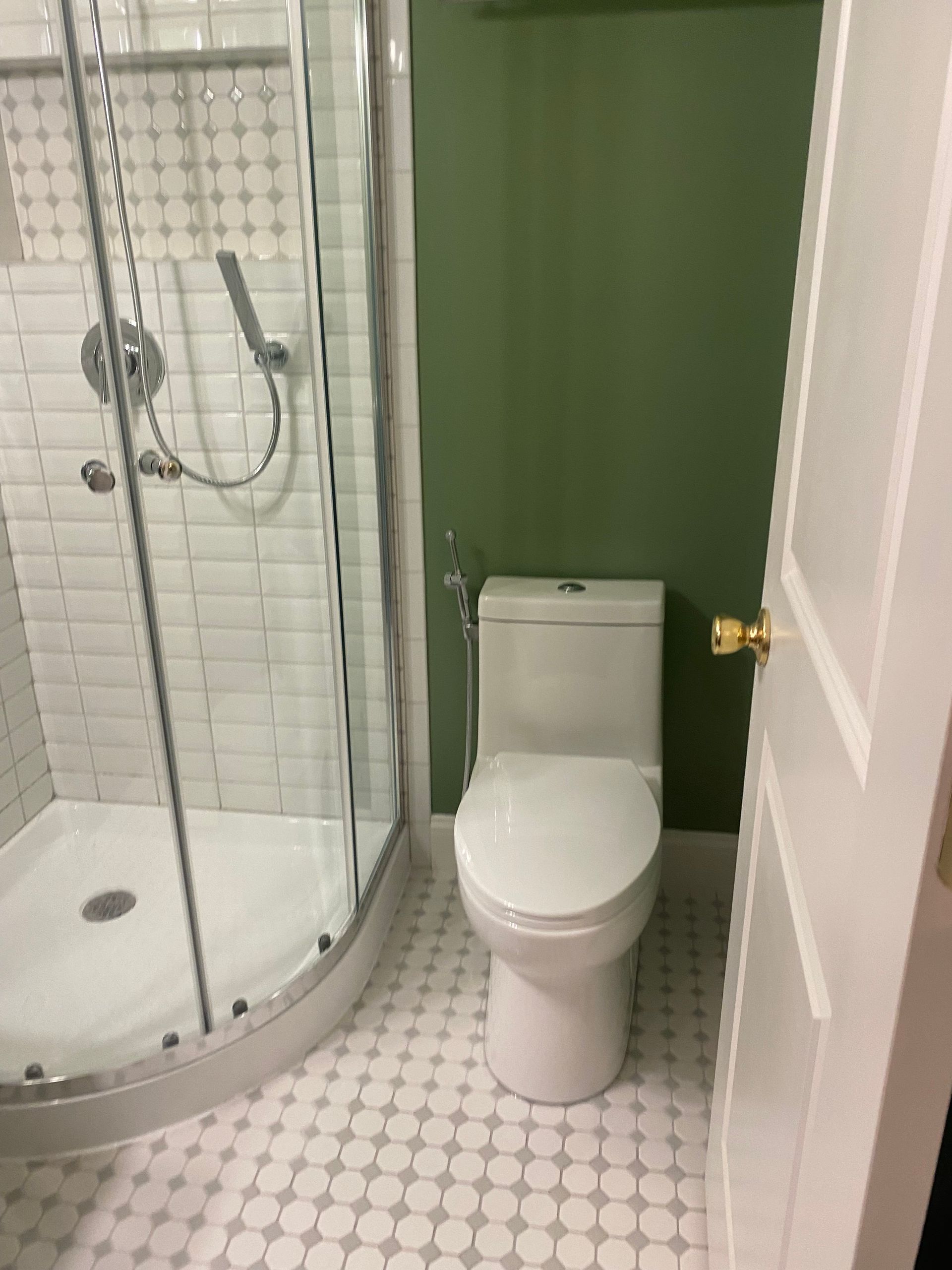 Small bathroom with shower, toilet, and open door; white tile floor and green wall.