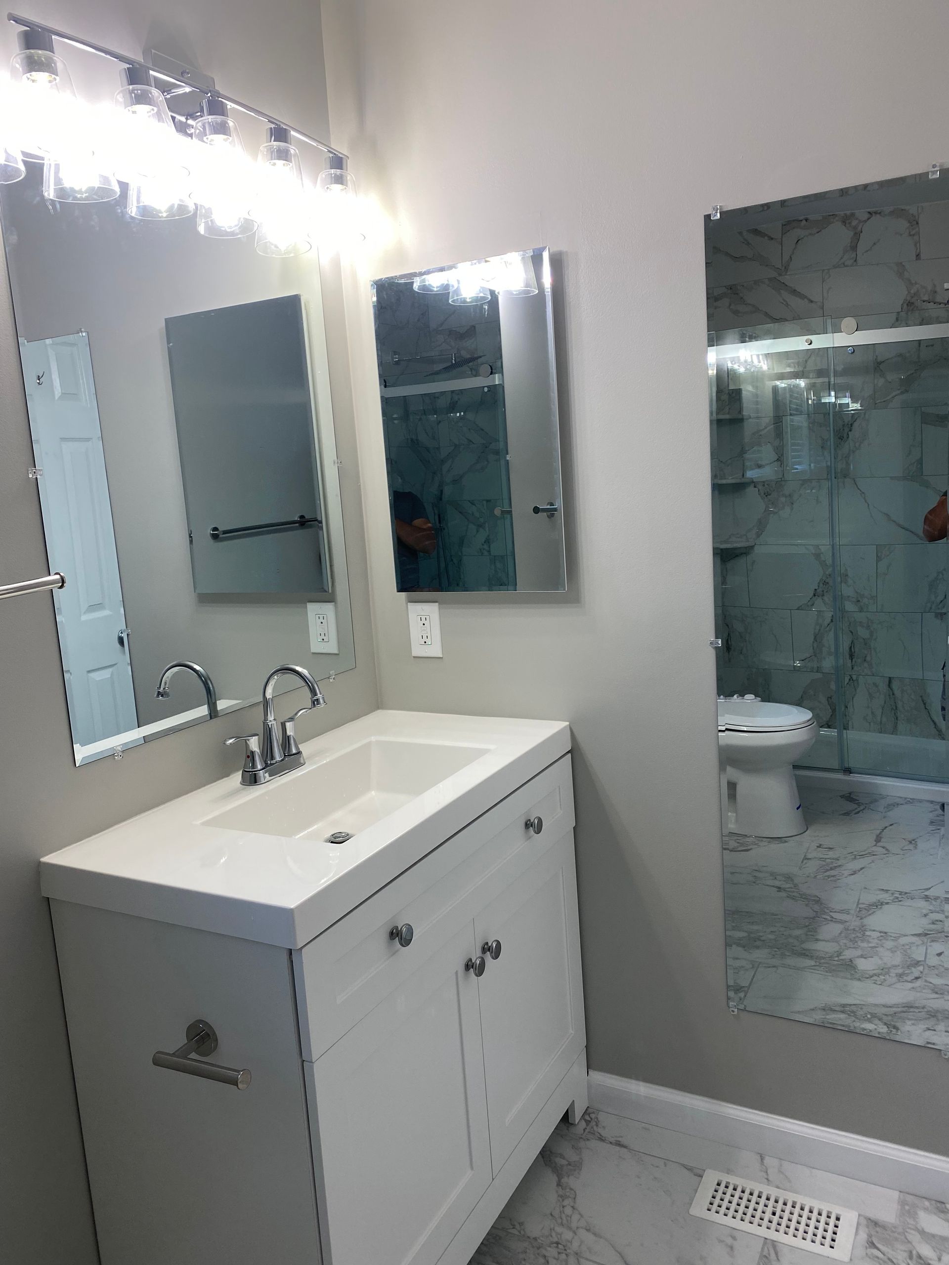Modern bathroom vanity with mirror, sink, and glass shower door under bright lights