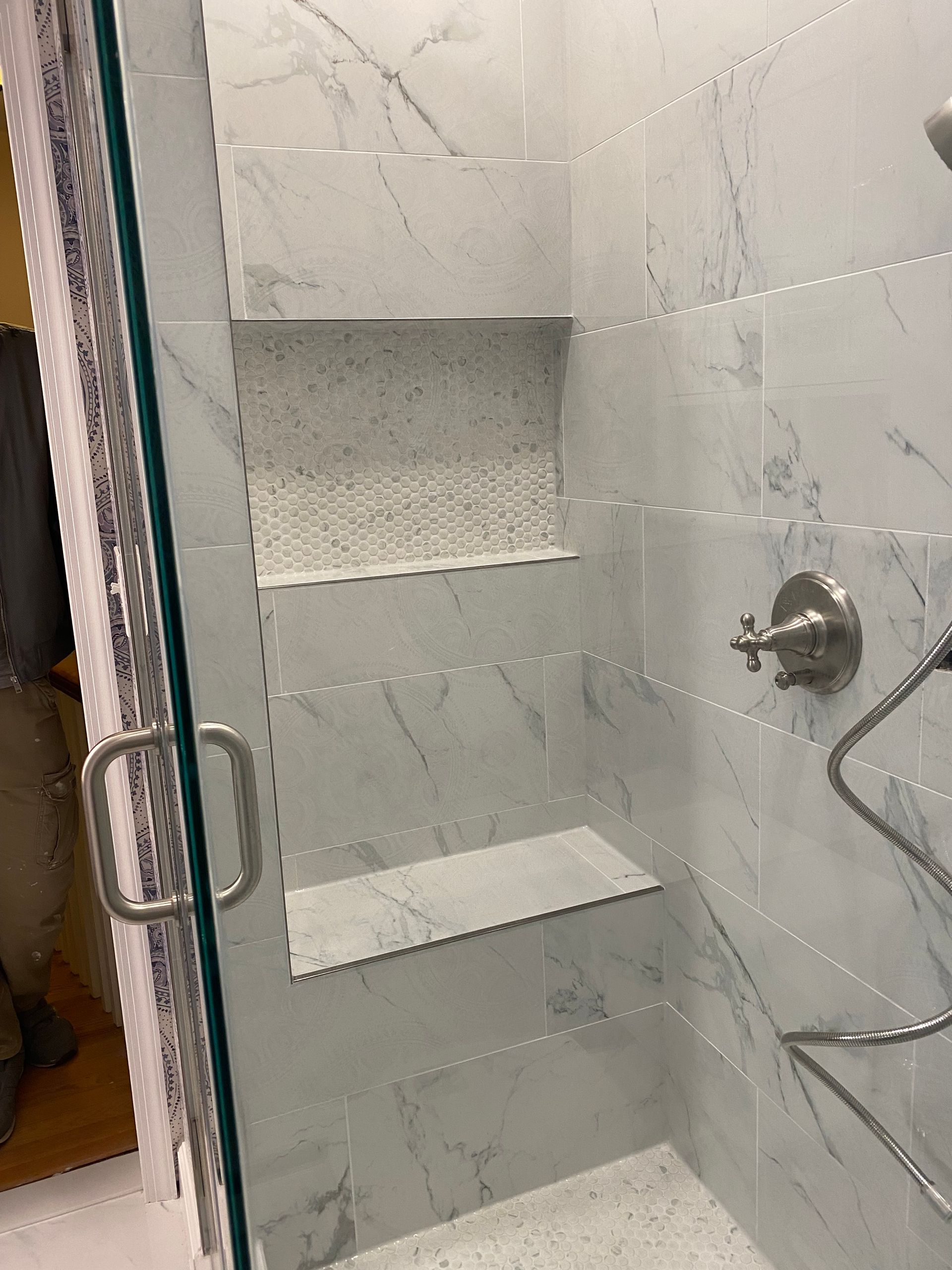 Tiled walk-in shower with built-in niches, glass door, and chrome shower fixtures.
