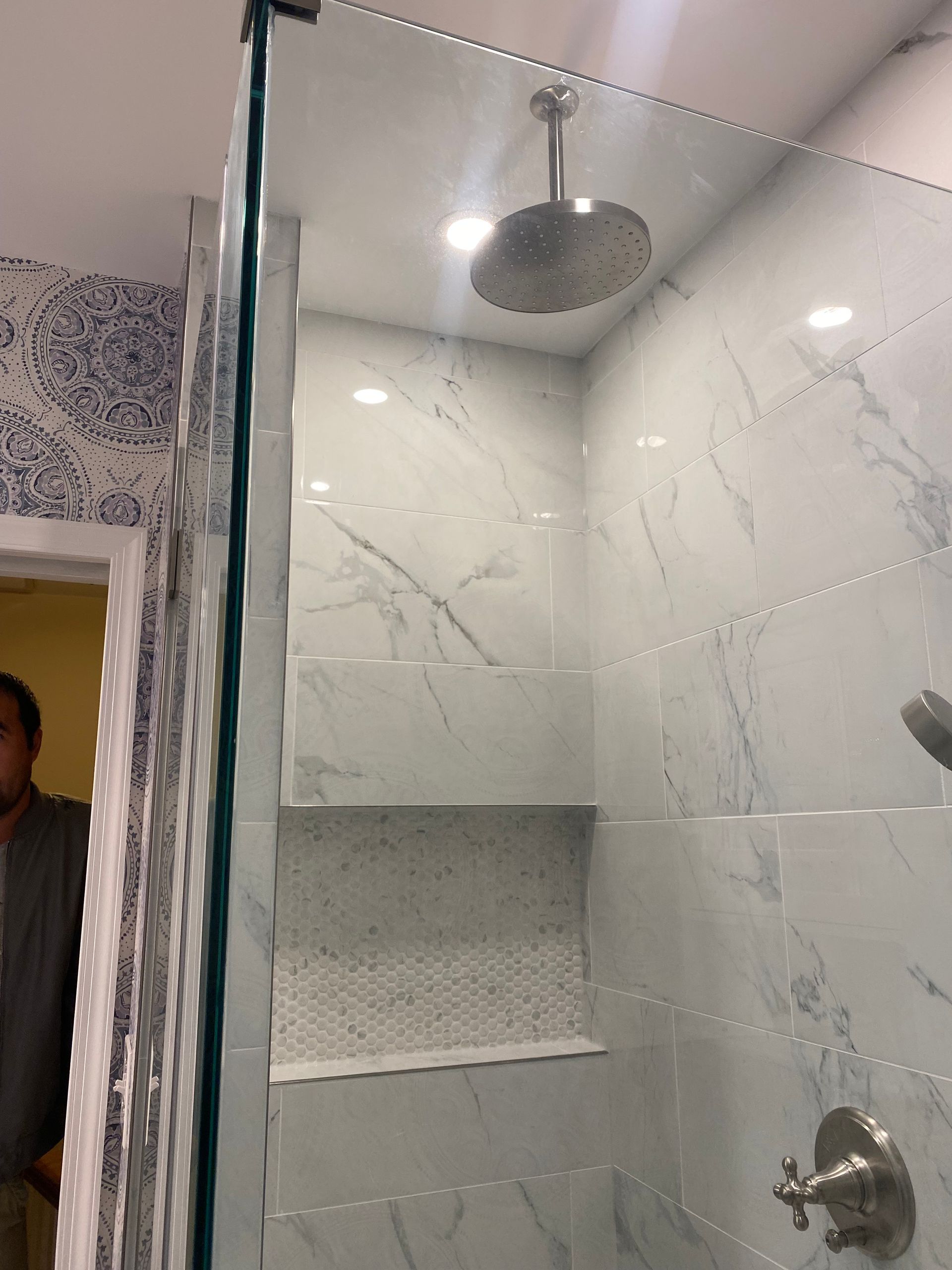 Modern marble-tile shower with glass door, built-in niche, and chrome rain showerhead