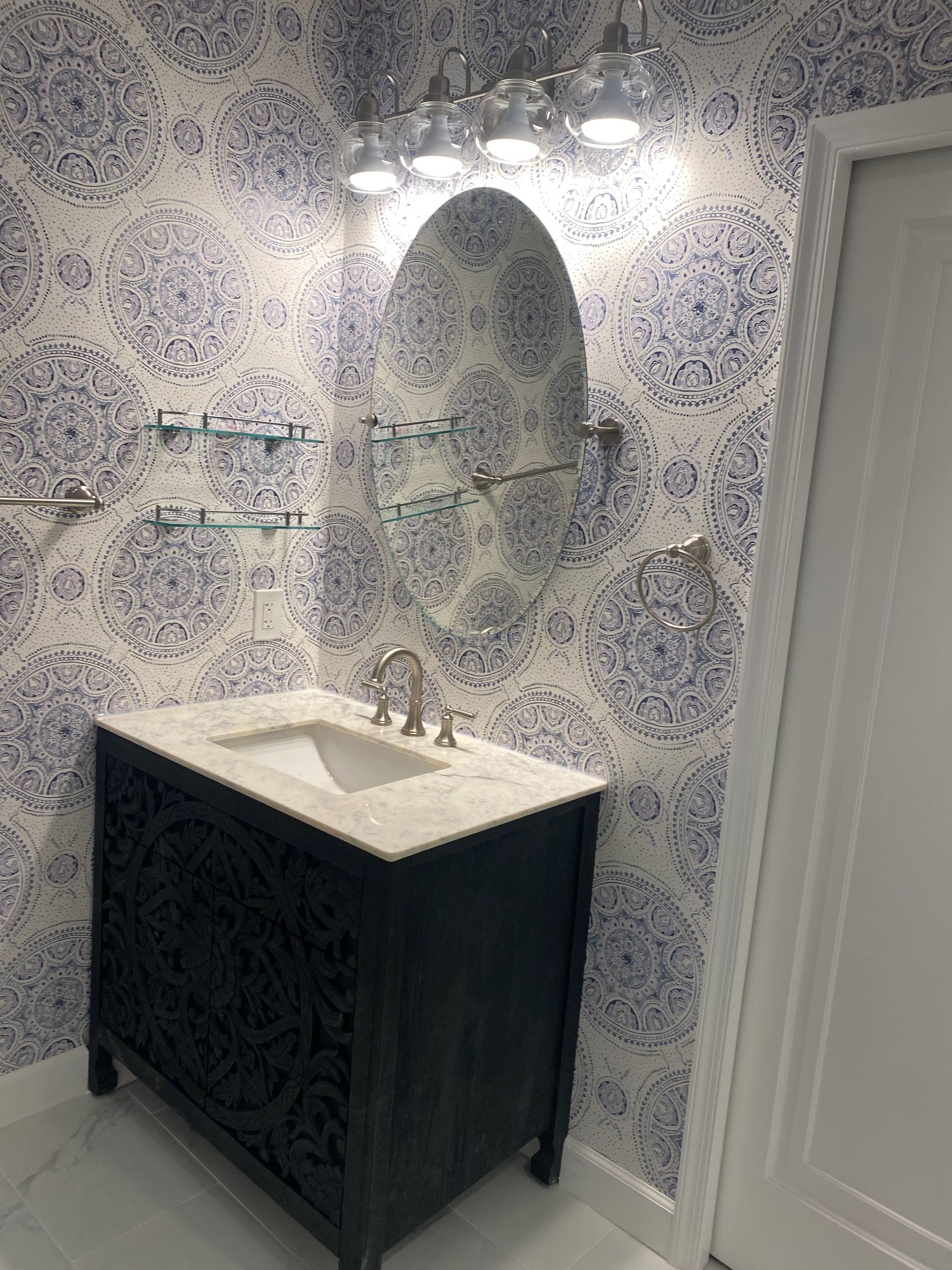 Compact bathroom vanity with white sink, black cabinet, arched mirror, and patterned blue wallpaper.