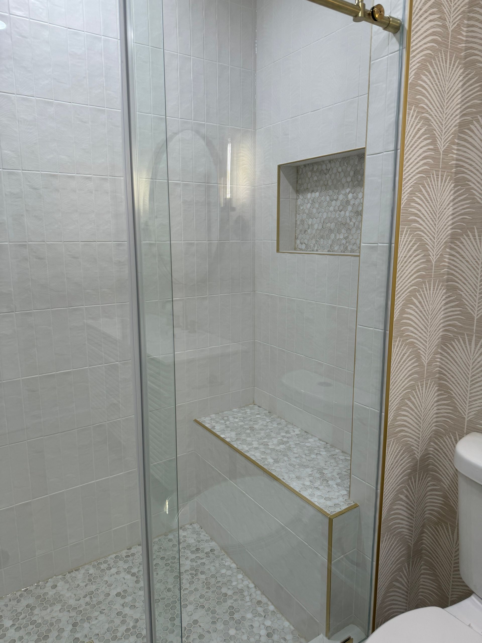 Glass shower enclosure with a built-in shelf and gray patterned tile walls