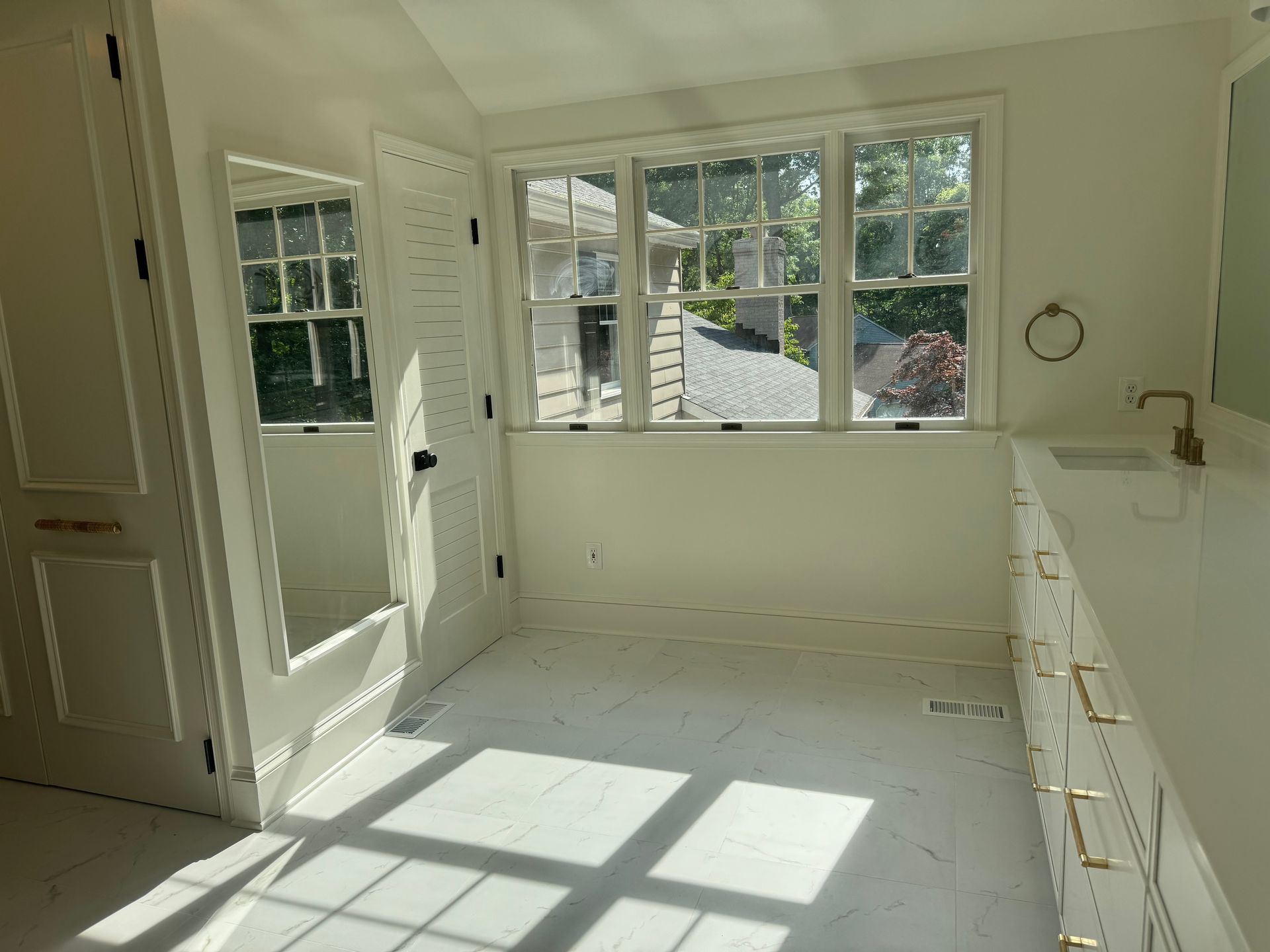 Bright sunlit white kitchen or laundry room with windows, cabinets, and an open door to outside.