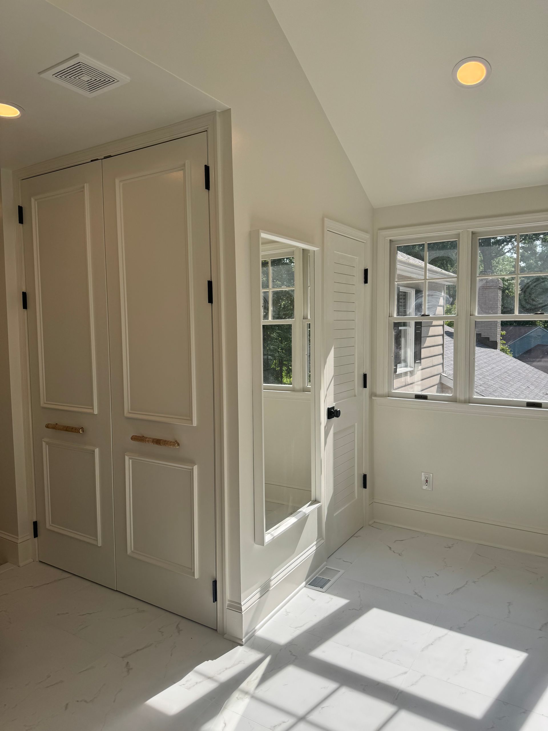 Bright empty room with white walls, double closet doors, and sunlight streaming through windows onto the floor.