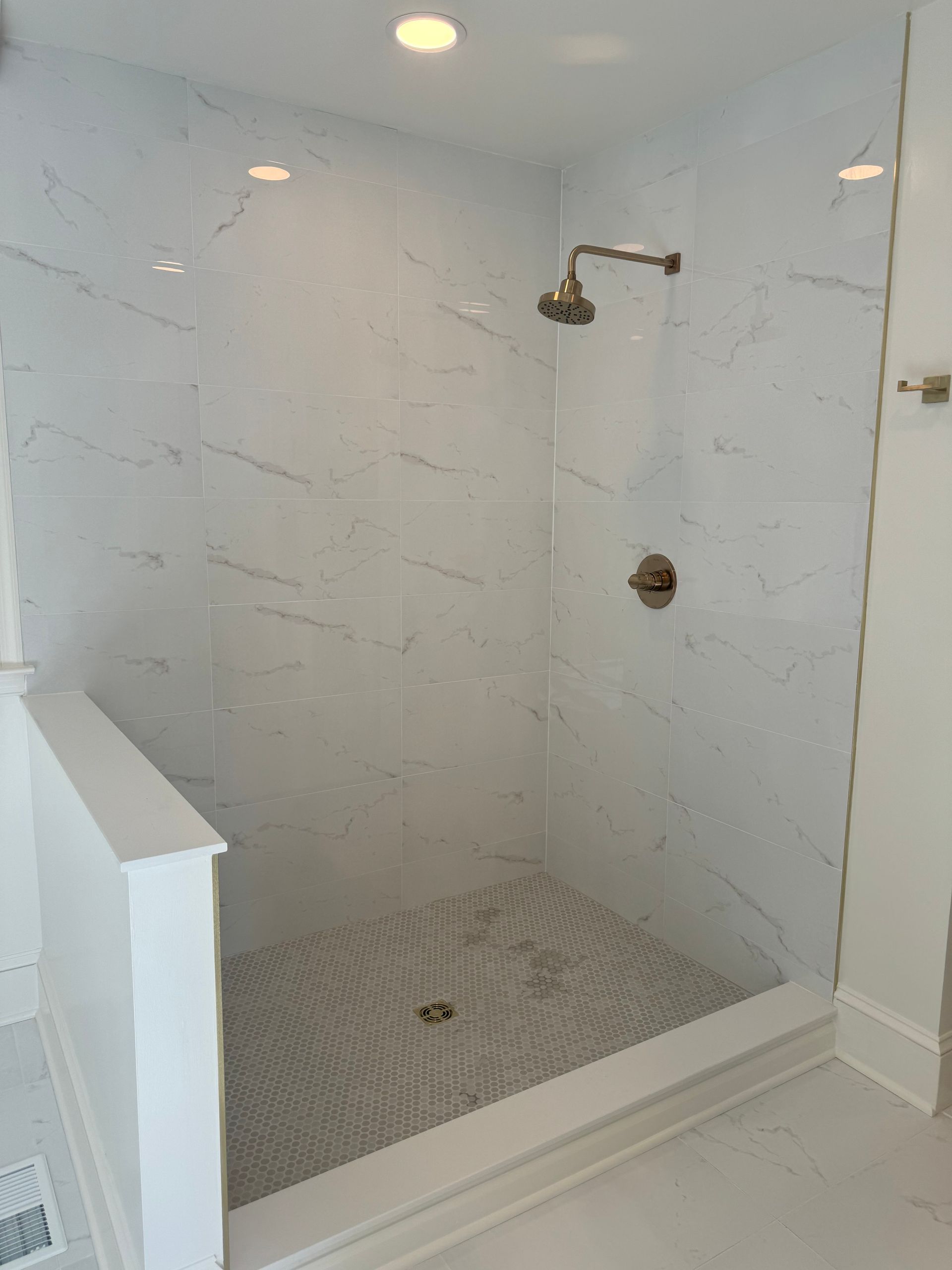 White tiled walk-in shower with a handheld showerhead and pebble floor behind glass wall