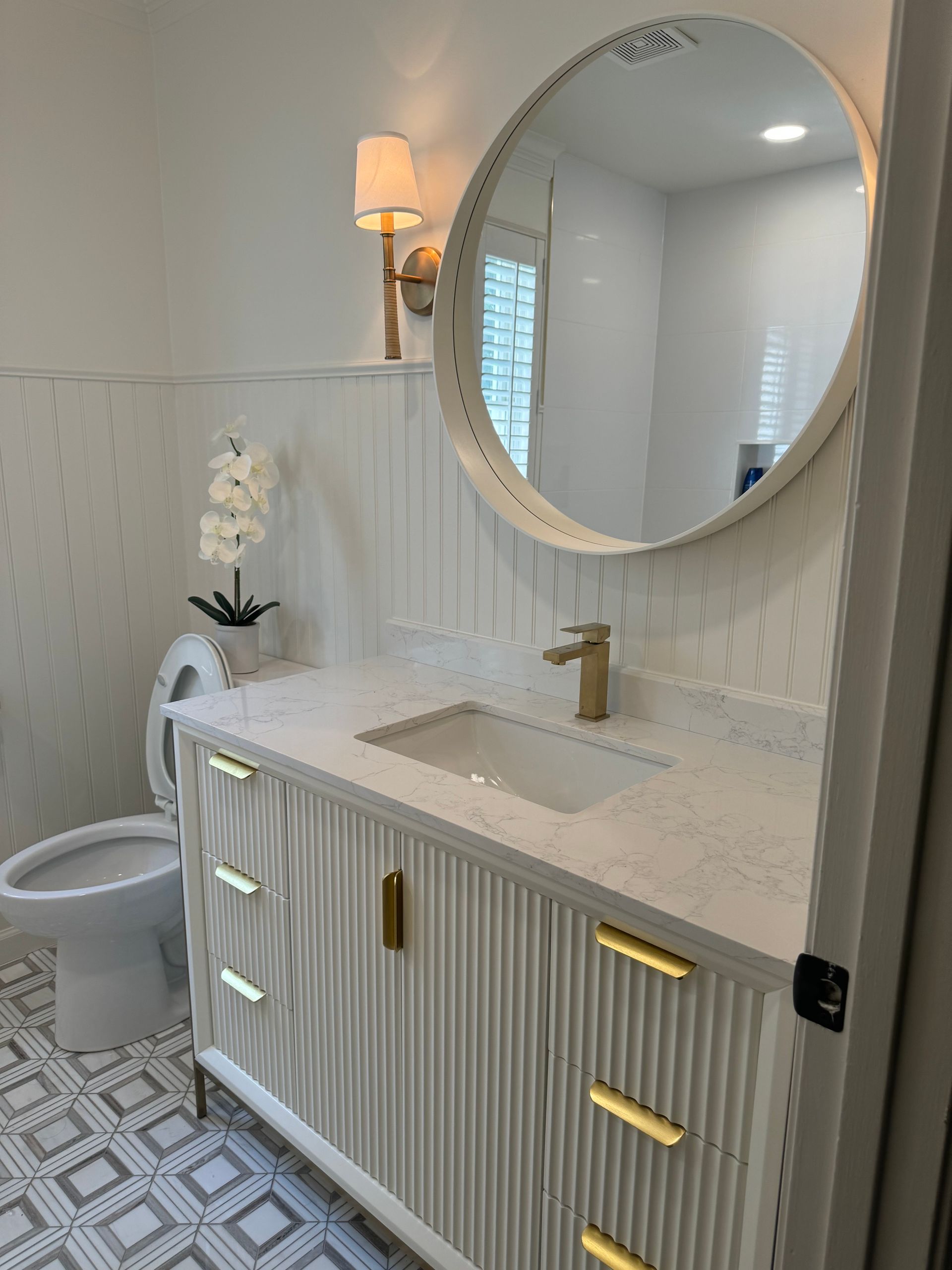 Bright bathroom vanity with round mirror, gold fixtures, and patterned floor tiles