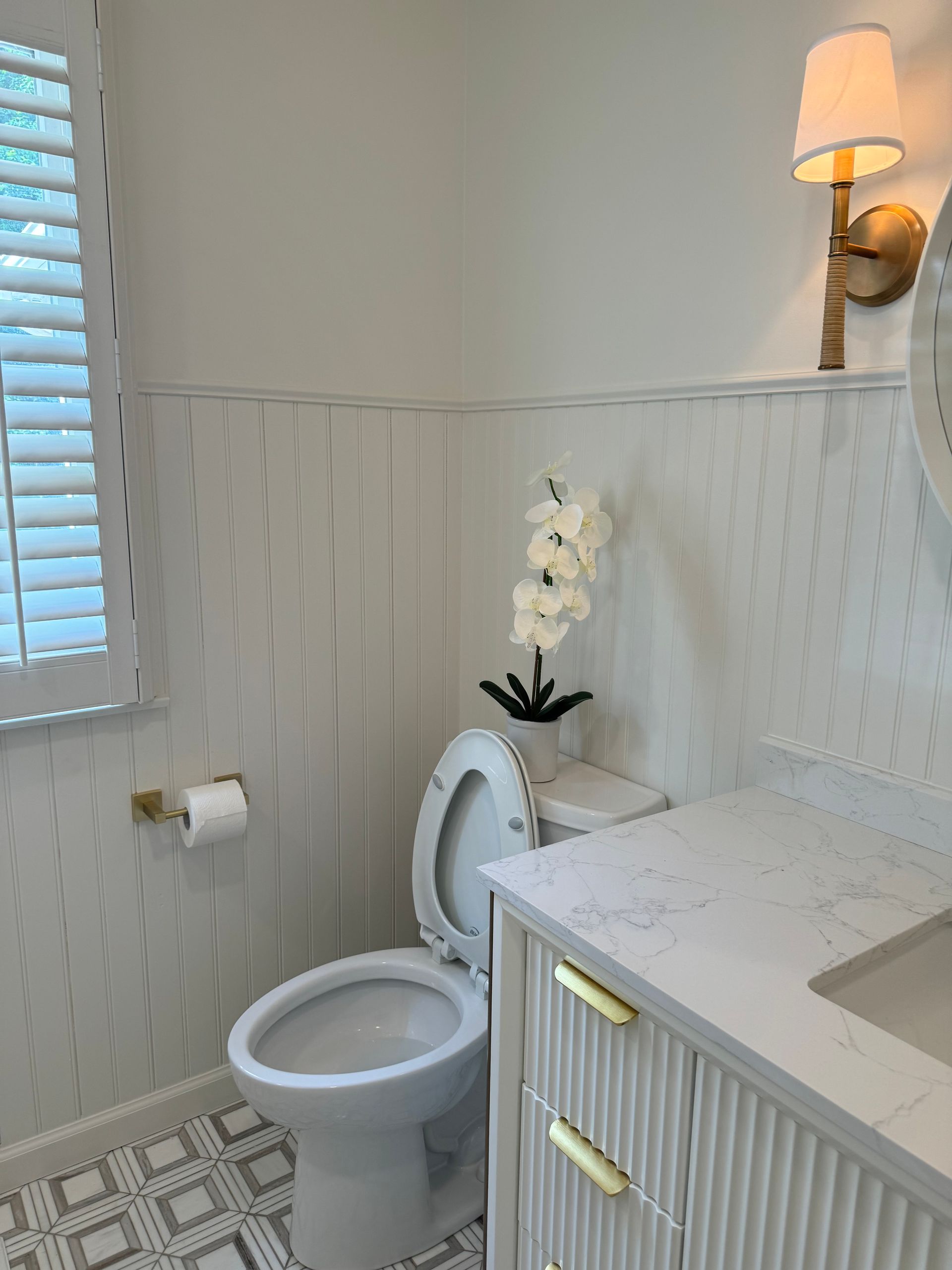 Small bathroom with white toilet, vanity, wall sconce, and window blinds.